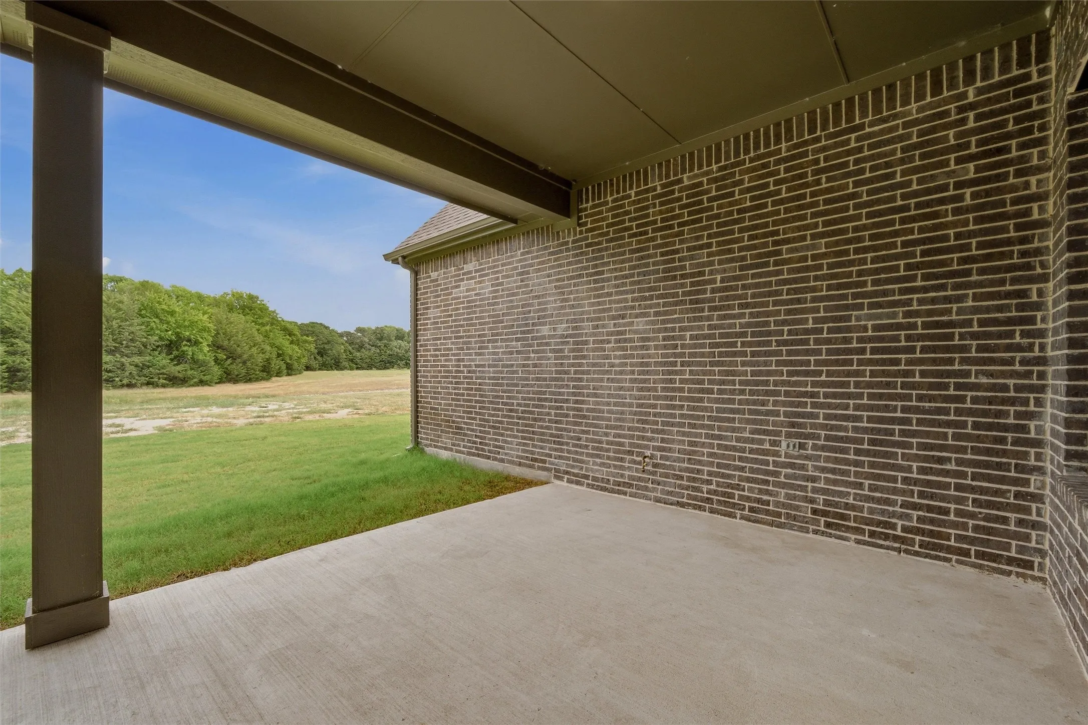 Covered concrete patio with brick exterior and expansive green space