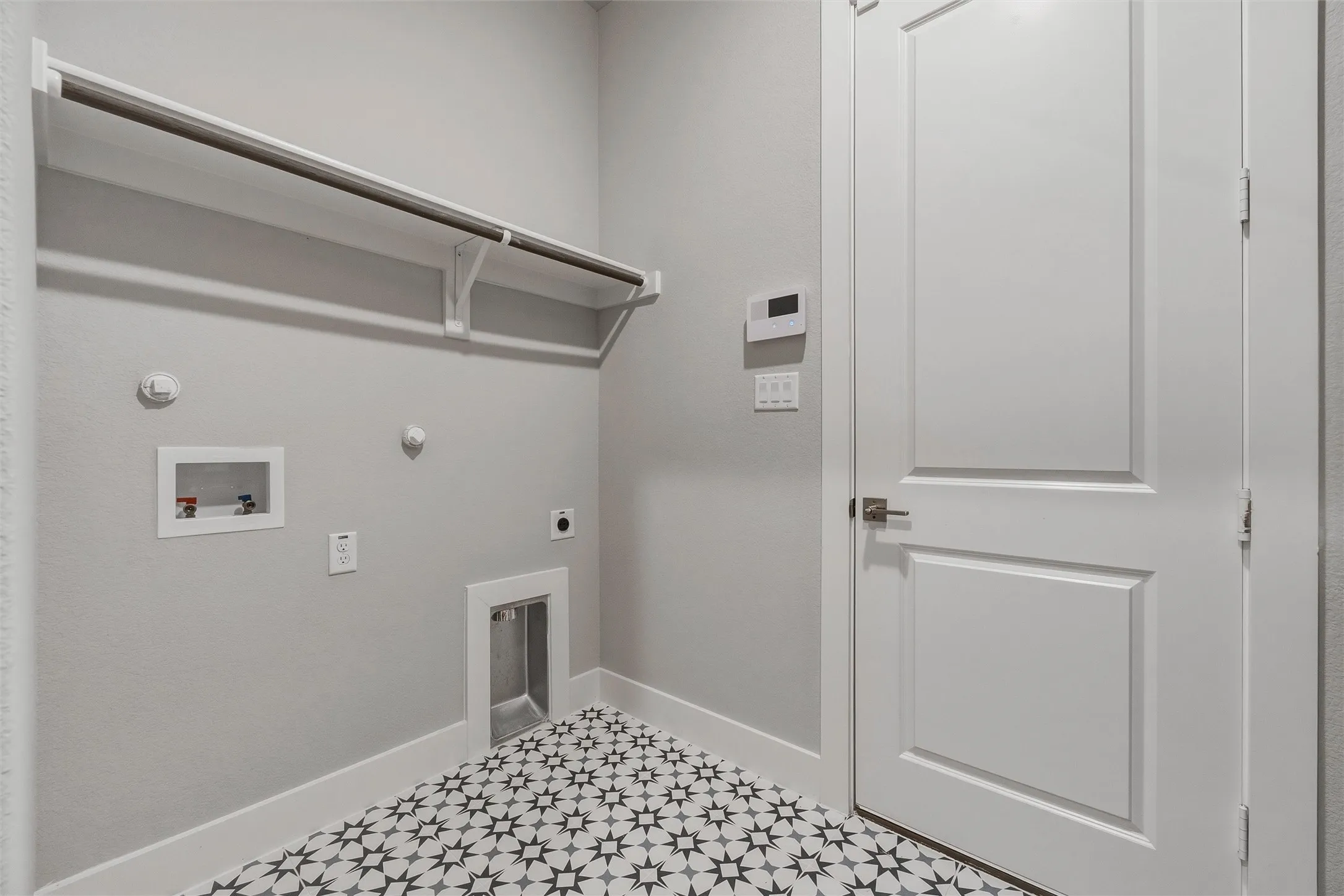 Patterned floor tile, white baseboards, built-in shelving, panel door, and wall-mounted controls