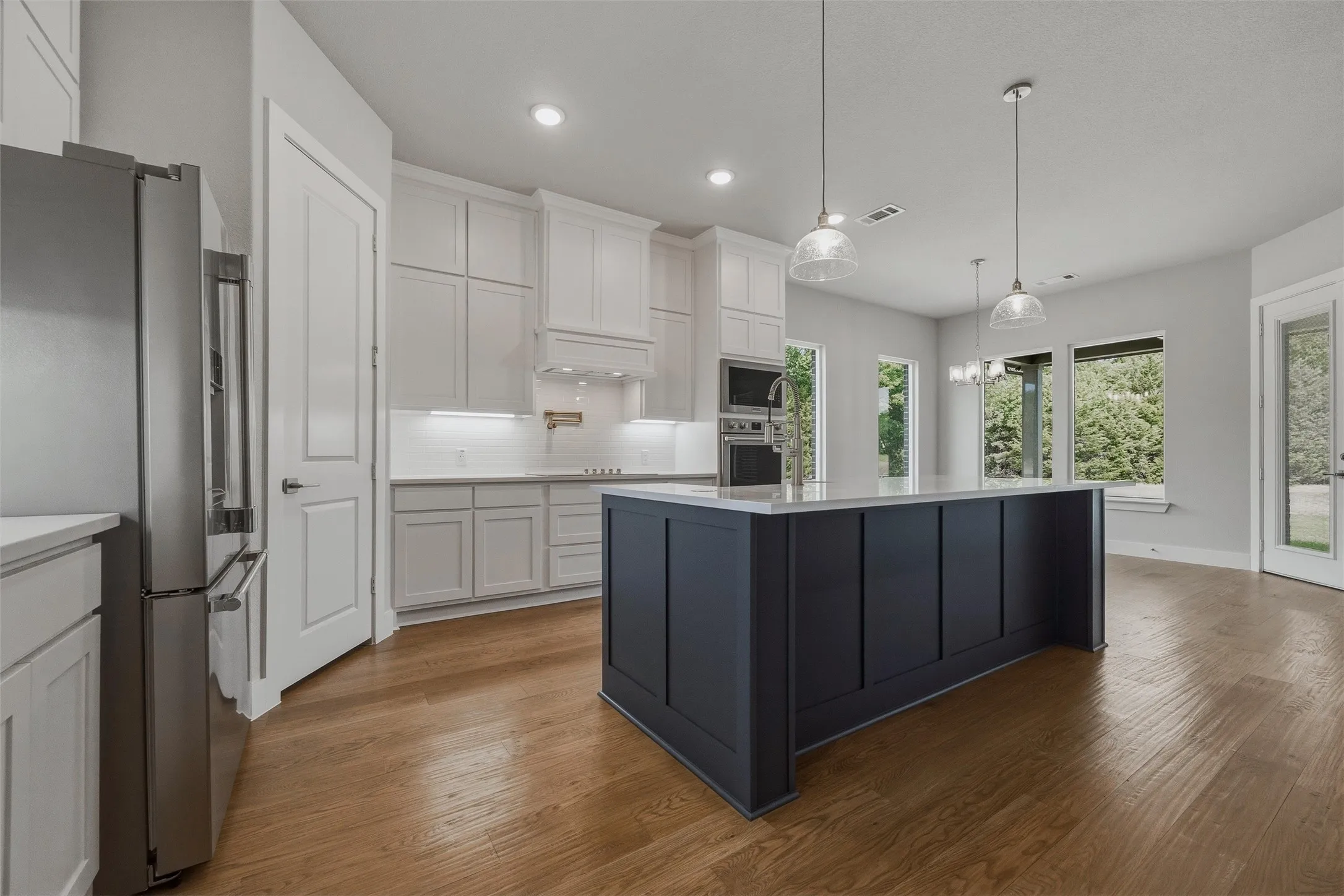 Gourmet kitchen with wood-finish flooring, white cabinetry, a dark-toned island with integrated sink, stainless steel appliances, and pendant lighting