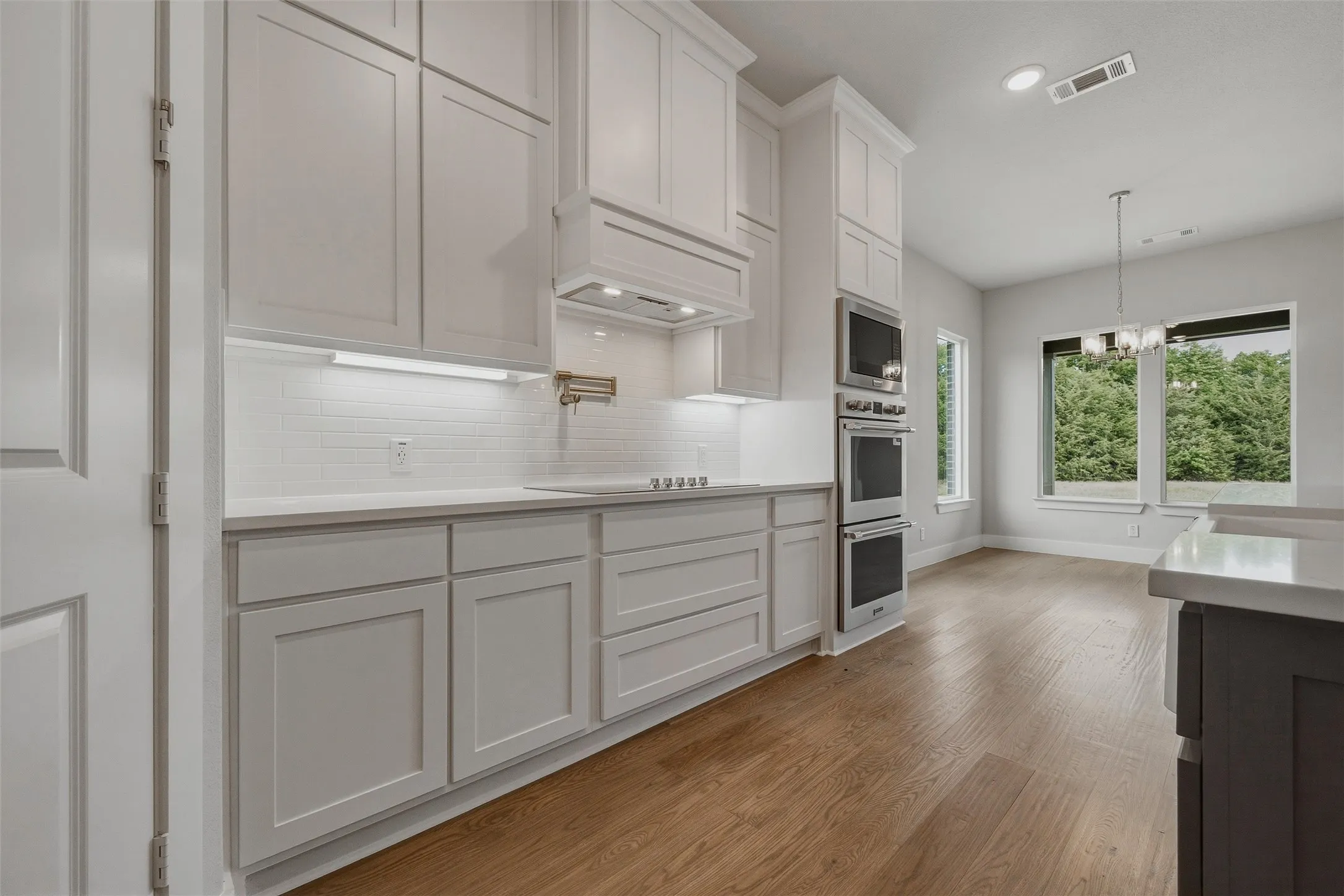Contemporary kitchen with white shaker cabinetry, stainless steel double ovens, wood-finish flooring, white subway tile backsplash, and recessed lighting