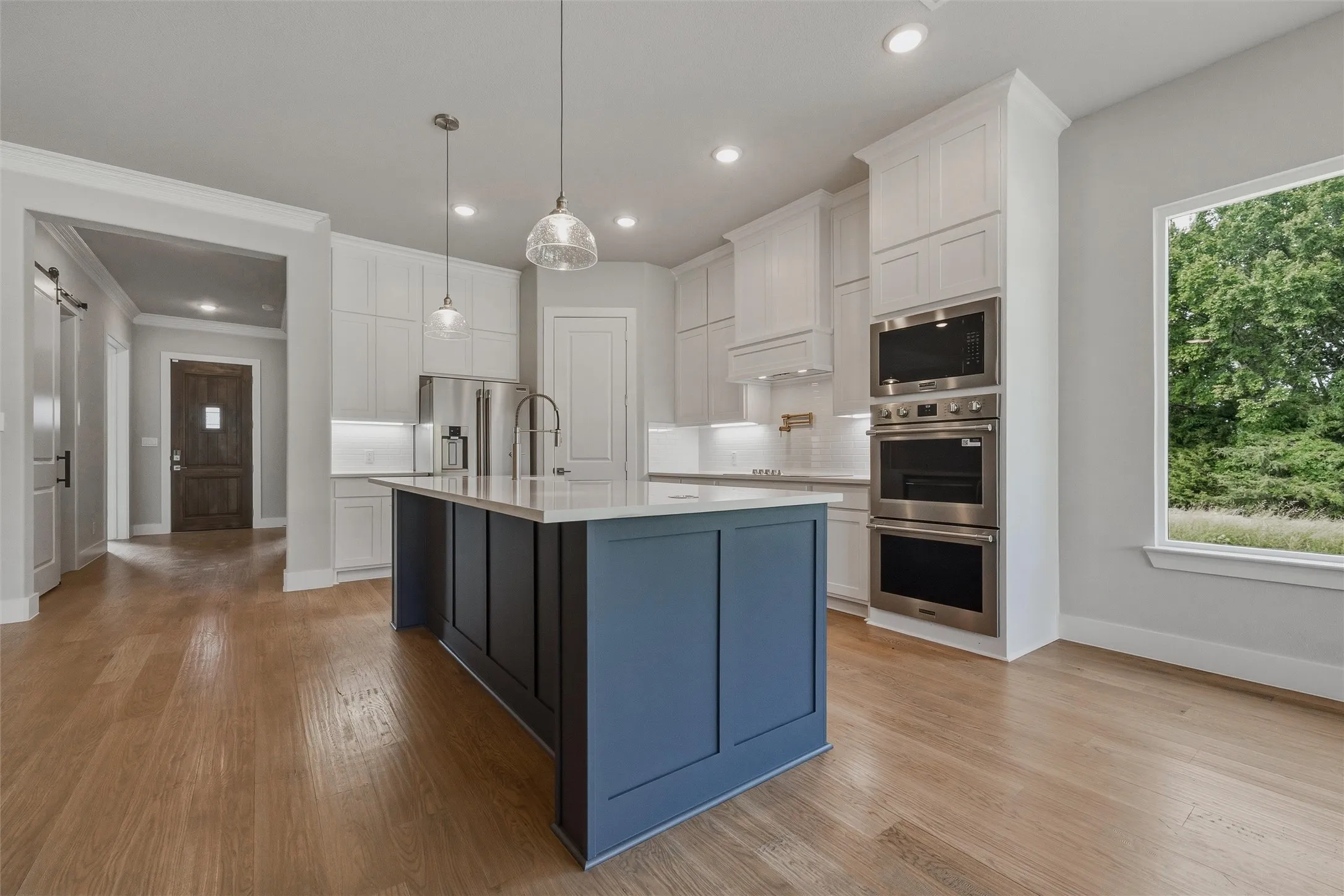 Kitchen featuring a blue-paneled island, light wood-finish flooring, white cabinetry, and stainless steel built-in appliances