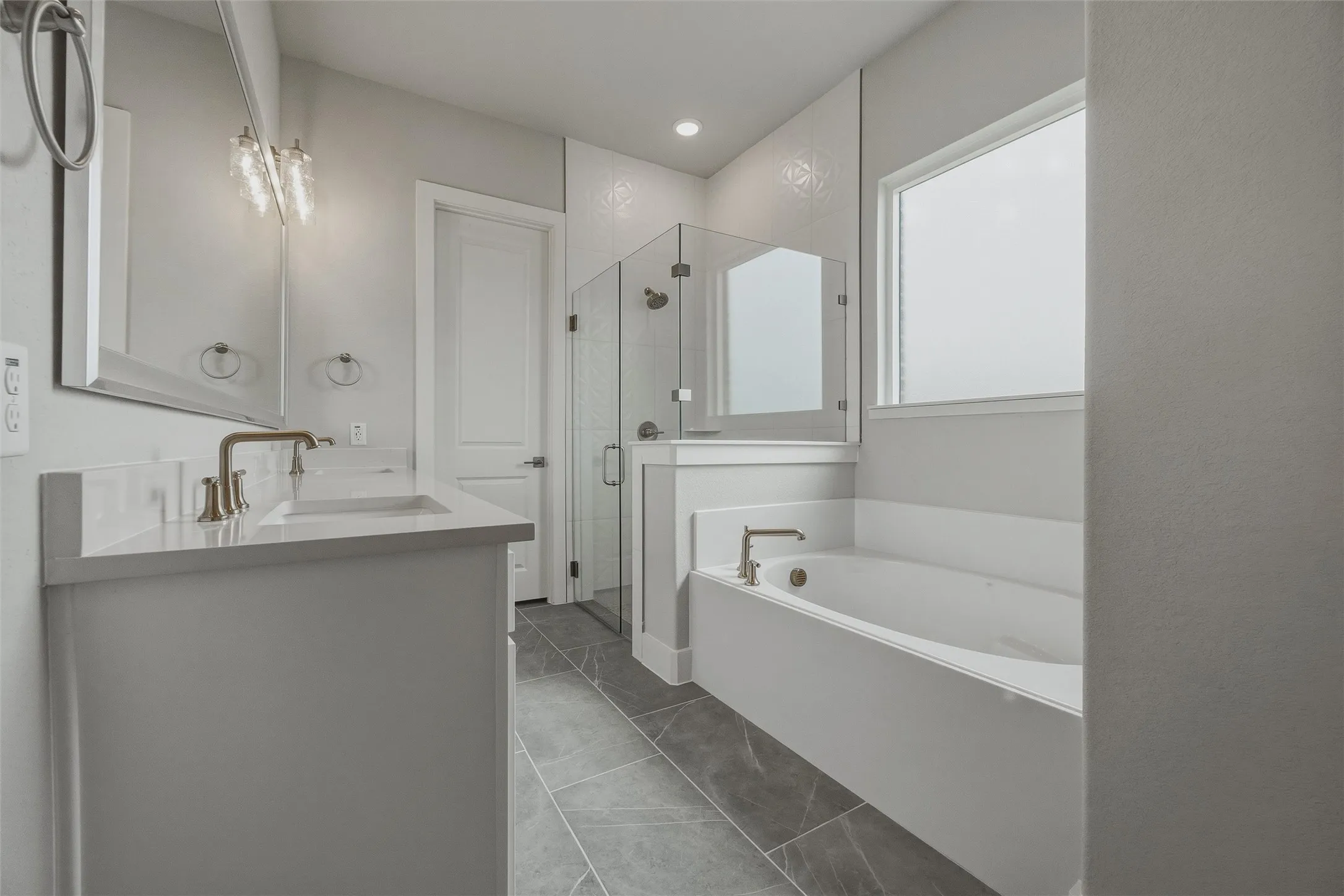 Dual vanity with integrated sinks, brushed nickel fixtures, a built-in soaking tub, a glass-enclosed shower, and gray tile flooring