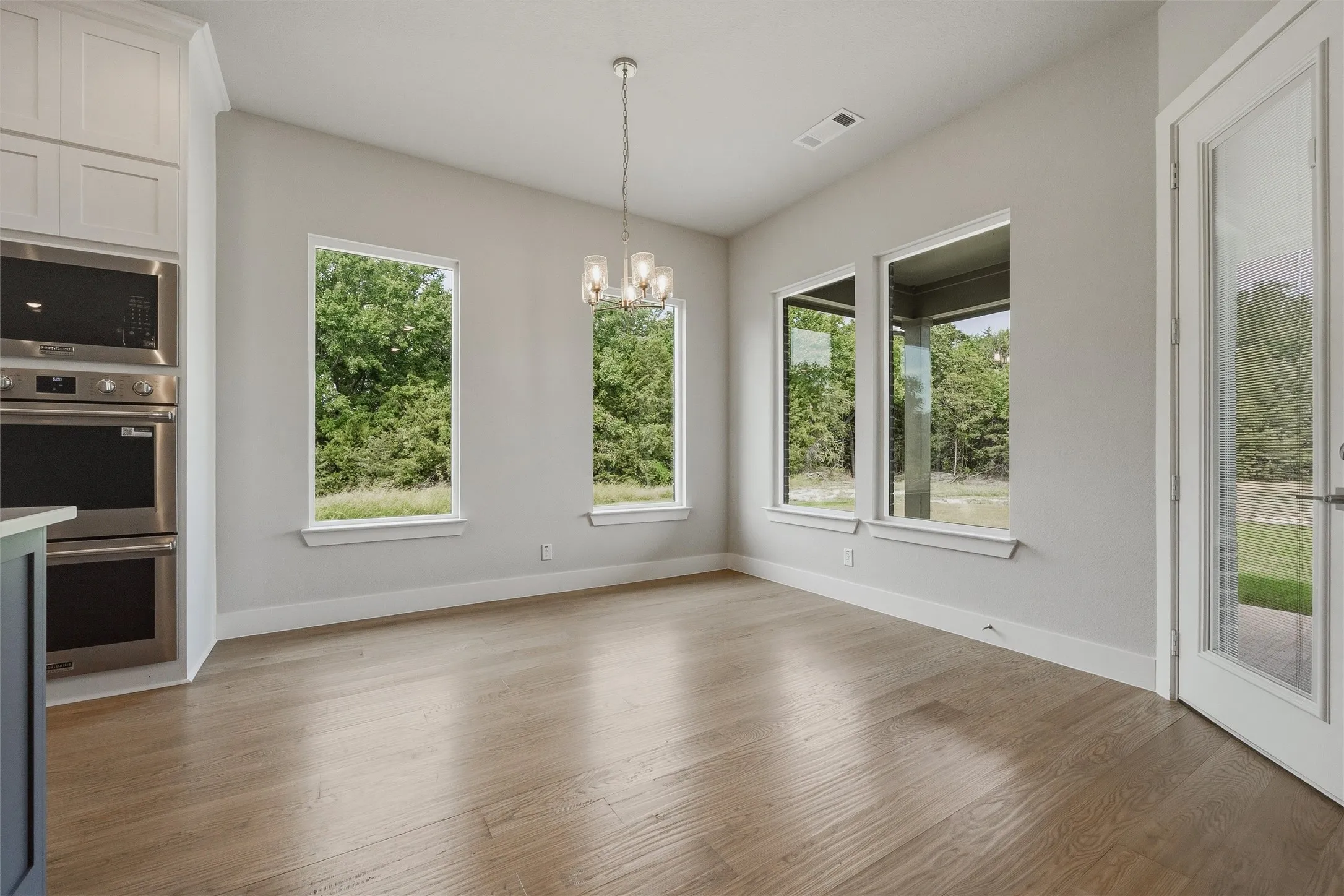 Wood-finish flooring, multiple large windows, recessed lighting, built-in double ovens, and a contemporary chandelier