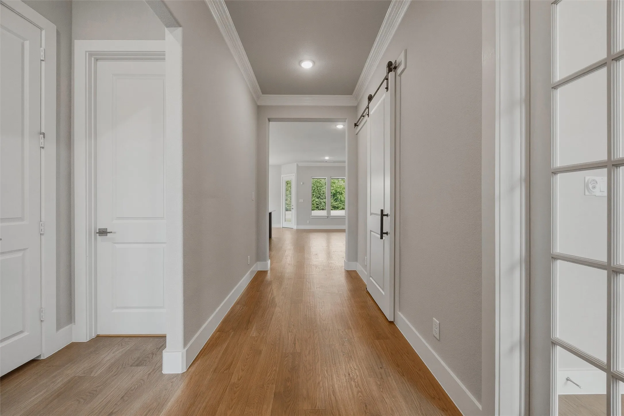 Hardwood-style flooring throughout, crown molding, recessed lighting, white trim, and a modern barn door