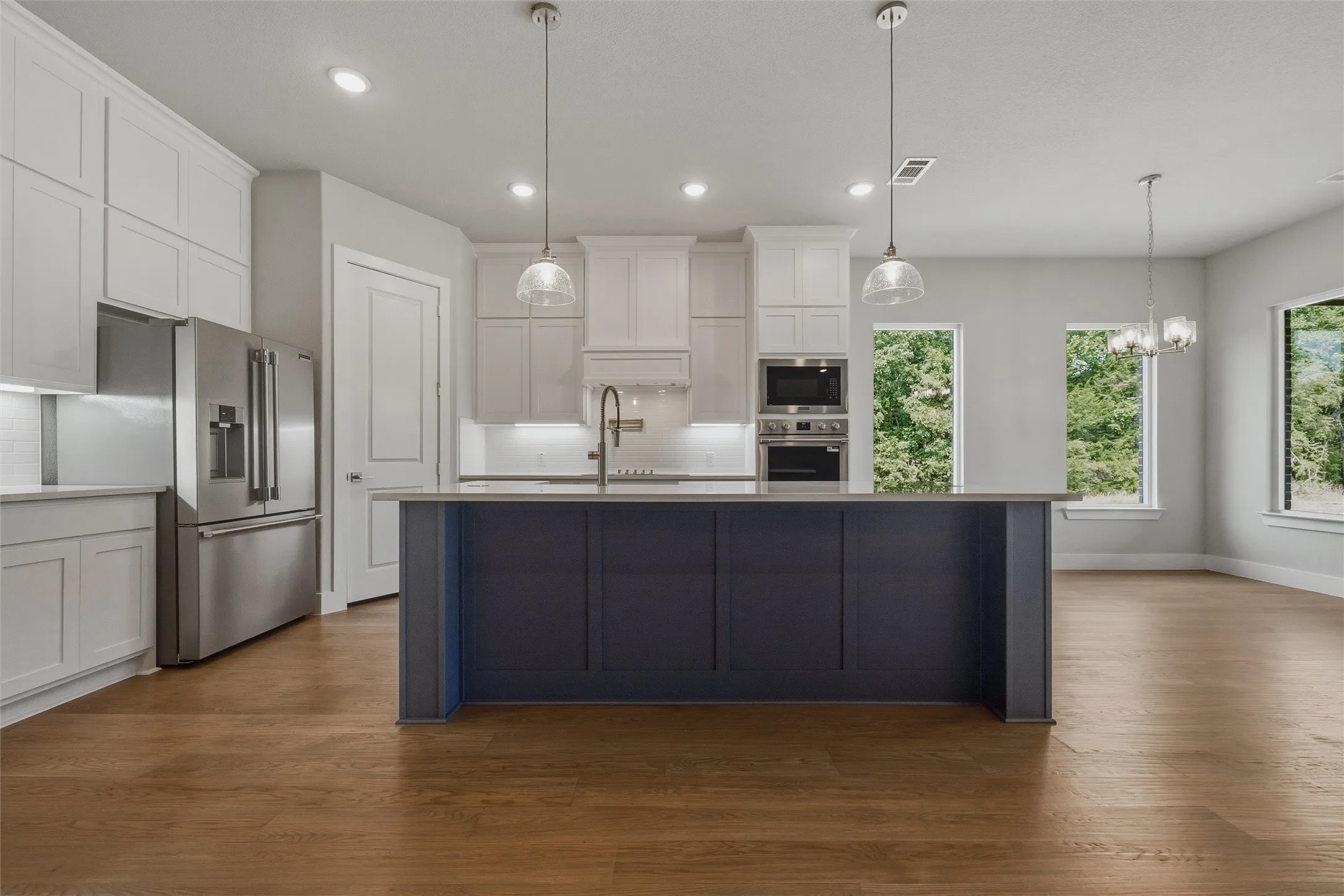 Kitchen featuring a two-toned island, stainless steel appliances, wood-finish flooring, recessed lighting, and pendant fixtures