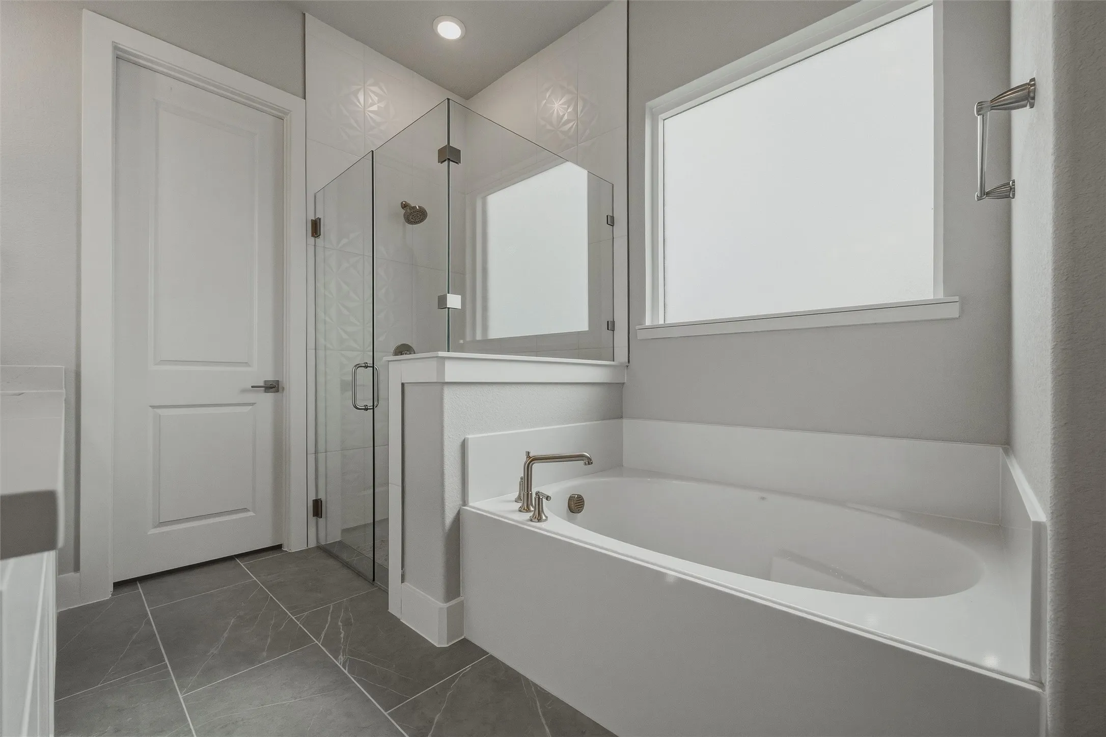 Built-in soaking tub with deck-mounted faucet, glass-enclosed shower with tile surround, and large-format floor tiles