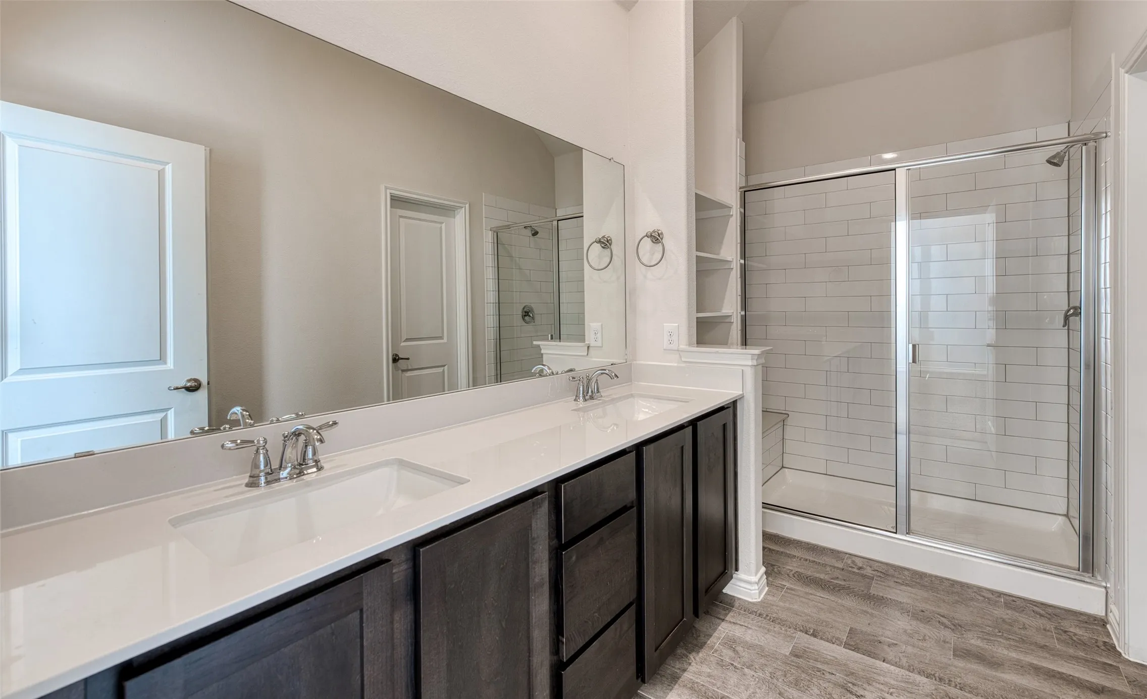 Full bathroom featuring double vanity, a stall shower, and light wood-style floors