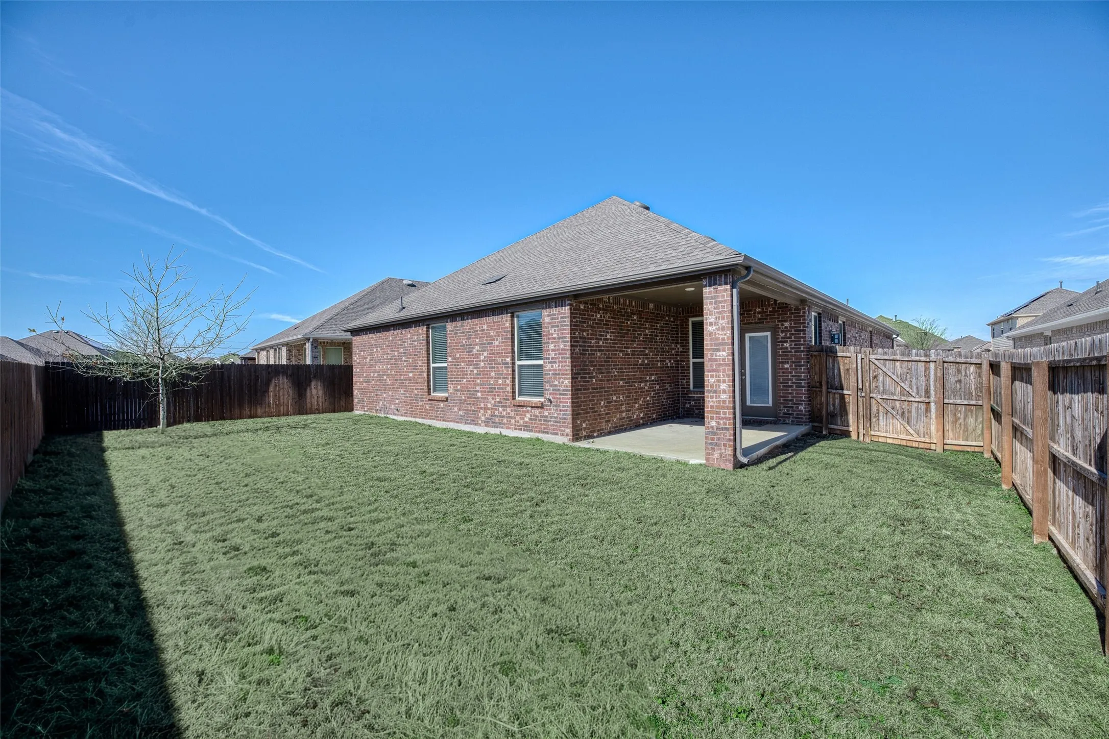 Rear view of property with a patio area, brick siding, a fenced backyard, and a shingled roof