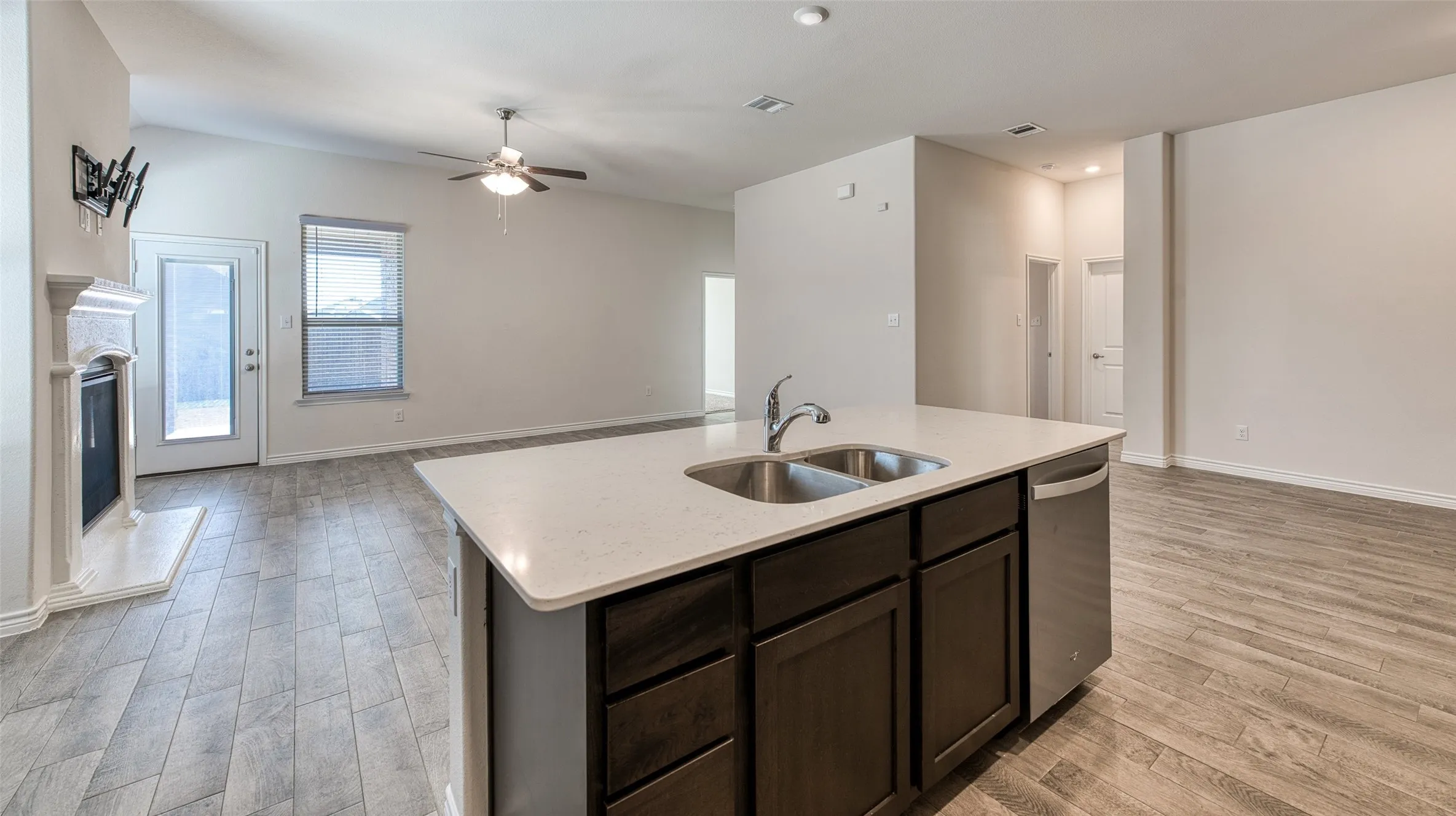 Kitchen with open floor plan, dark wood finish cabinets, light wood finished floors, stainless steel dishwasher, and ceiling fan