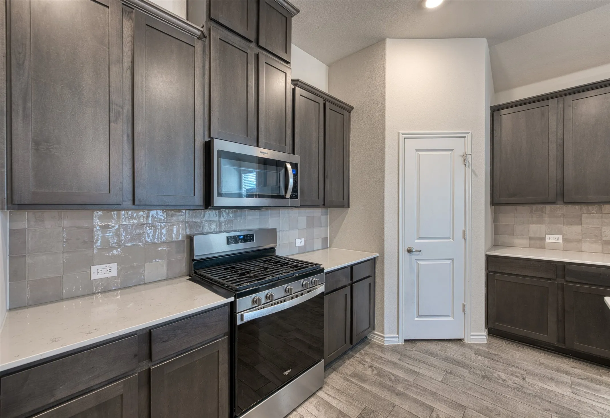 Kitchen featuring stainless steel appliances, decorative backsplash, light wood-style floors, and light stone countertops