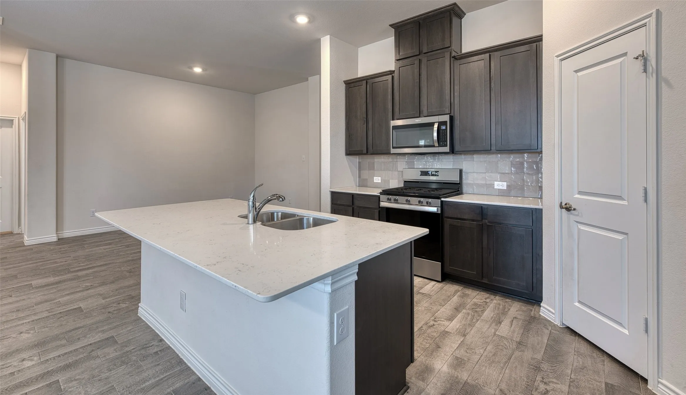 Kitchen with stainless steel appliances, decorative backsplash, light stone counters, light wood finished floors, and an island with sink