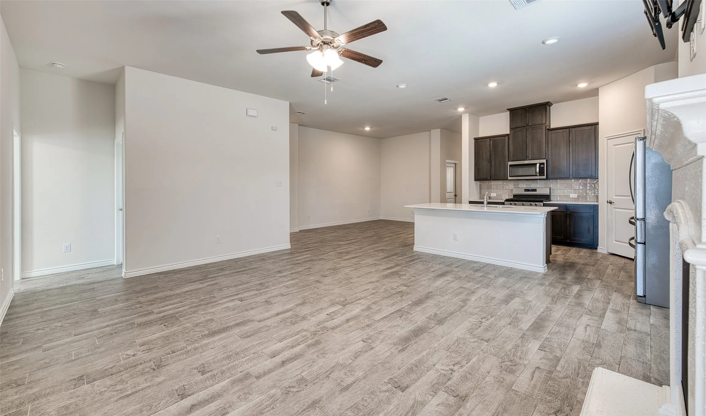 Kitchen featuring open floor plan, dark wood finish cabinets, a center island with sink, stainless steel appliances, and a ceiling fan