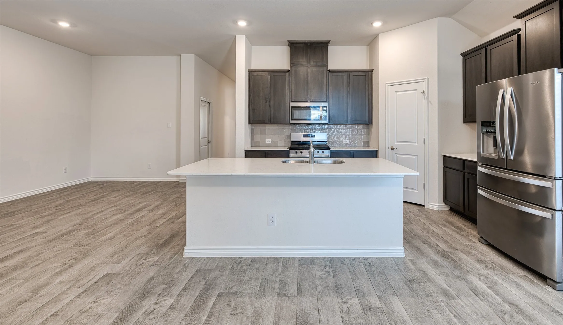 Kitchen with stainless steel appliances, a center island with sink, light wood-style floors, decorative backsplash, and dark wood finish cabinets