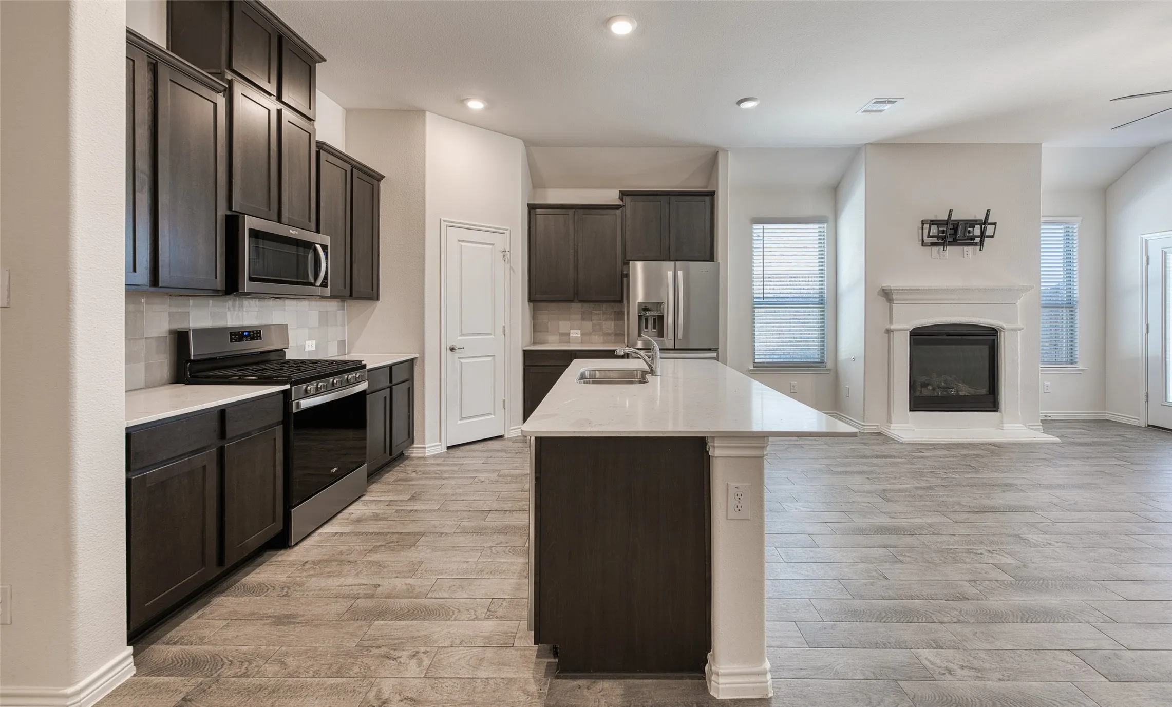 Kitchen featuring stainless steel appliances, open floor plan, tasteful backsplash, a kitchen island with sink, and a glass covered fireplace