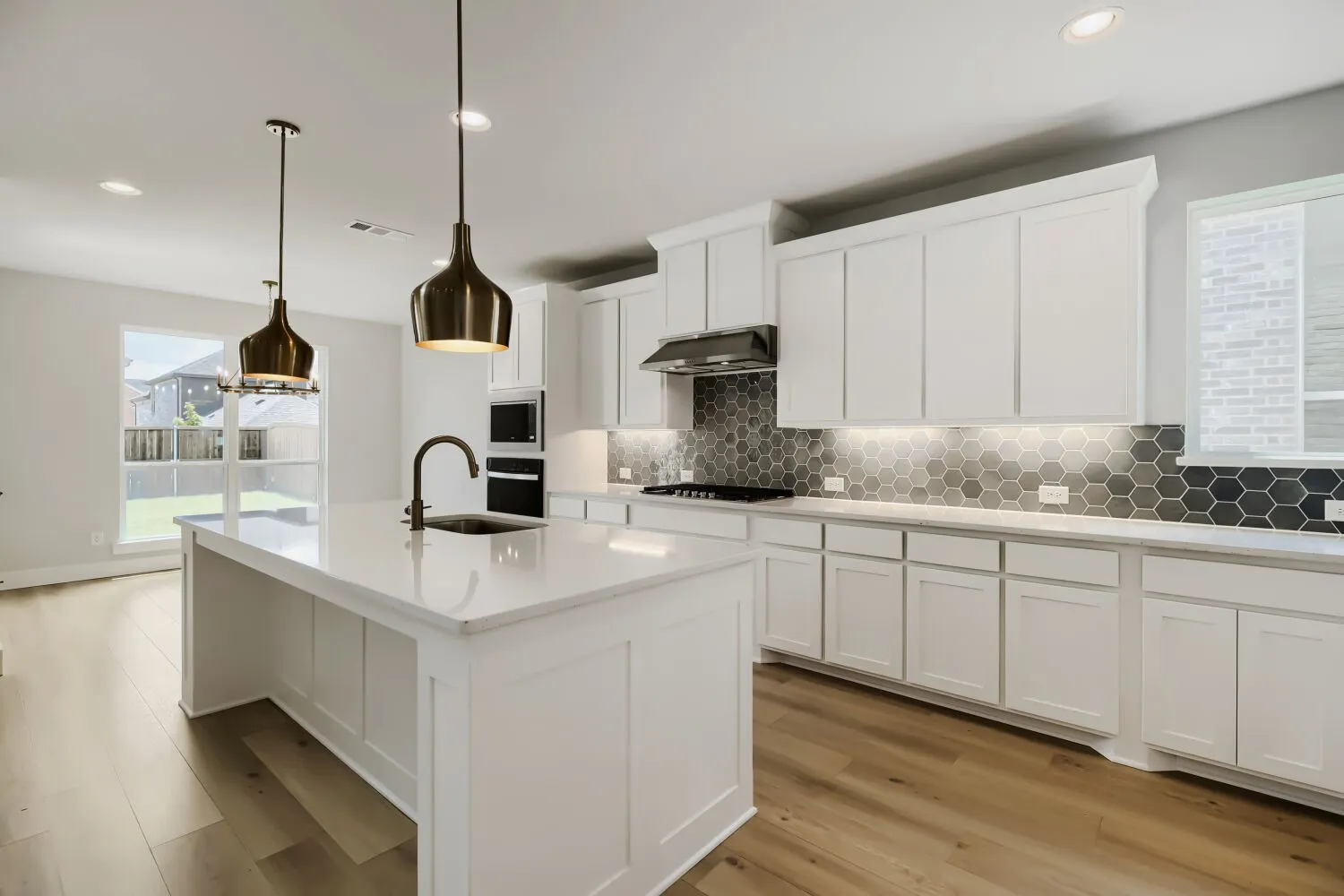 Modern kitchen featuring a large central island with integrated sink, white cabinetry, hexagon tile backsplash, and wood-finish flooring