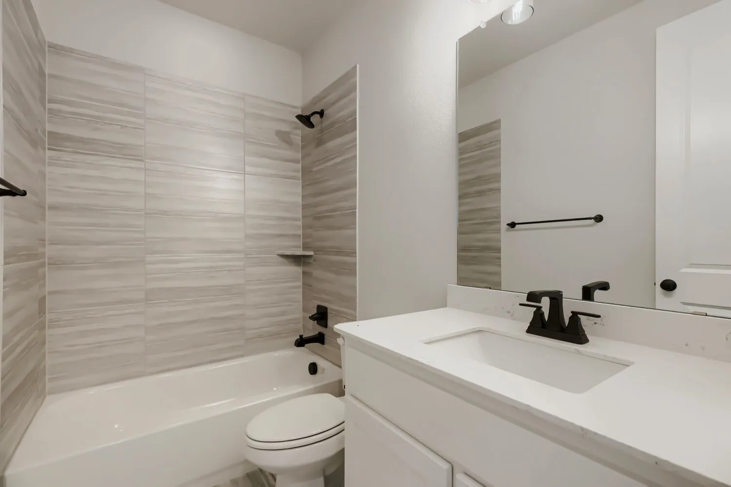 Bathroom featuring a tub/shower combination with horizontal tile surround, a single vanity with an integrated sink, a quartz-look countertop, and matte black fixtures