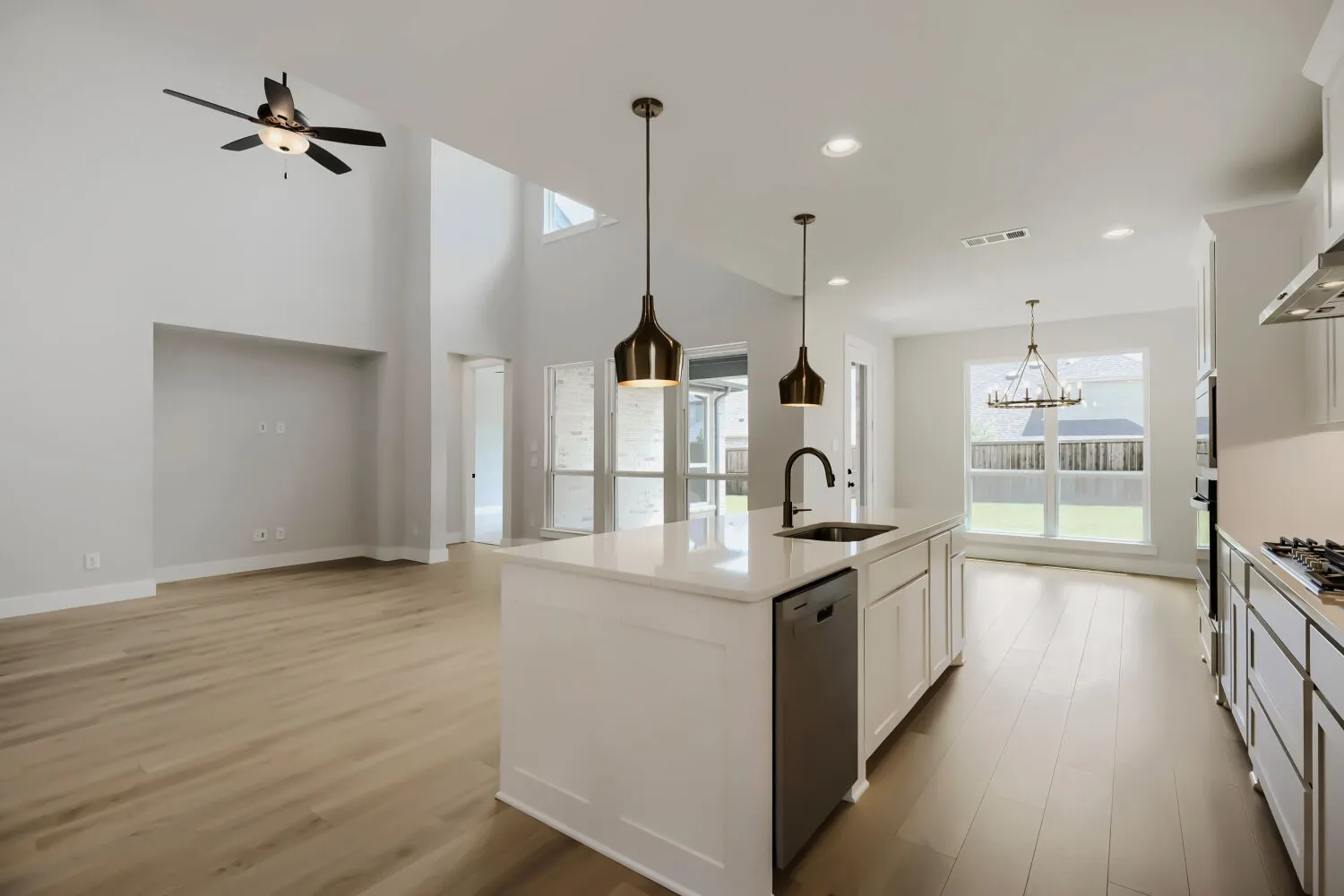 Open-concept kitchen and living area featuring a large center island with a built-in sink, pendant lighting, wood-finish flooring, and high ceilings
