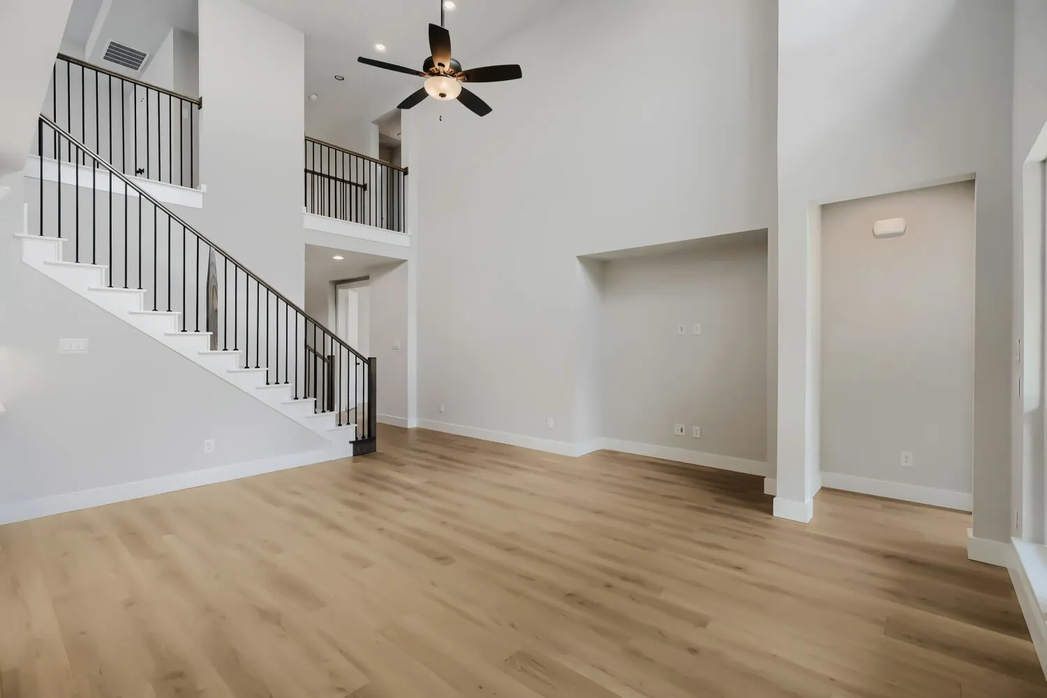 Two-story living area featuring wood-finish flooring, a contemporary staircase with black metal balusters and white risers, a built-in entertainment niche, and a ceiling fan with integrated lighting