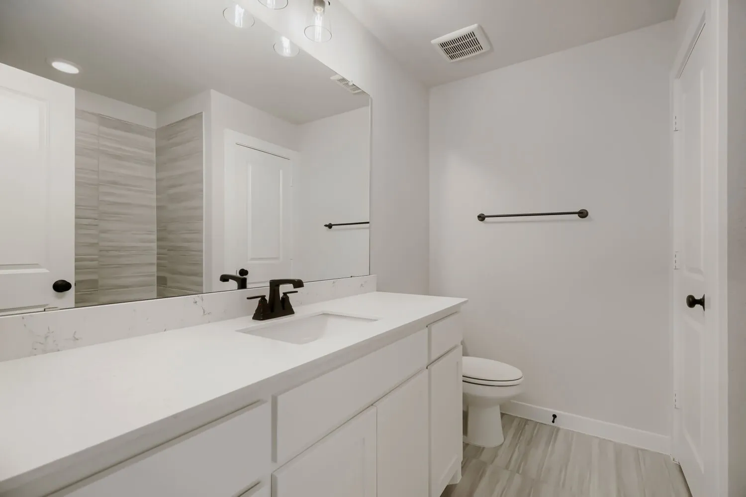Bathroom featuring an extended vanity with a solid surface countertop and undermount sink, matte black faucet, full-width mirror, and light wood-finish floor tiling