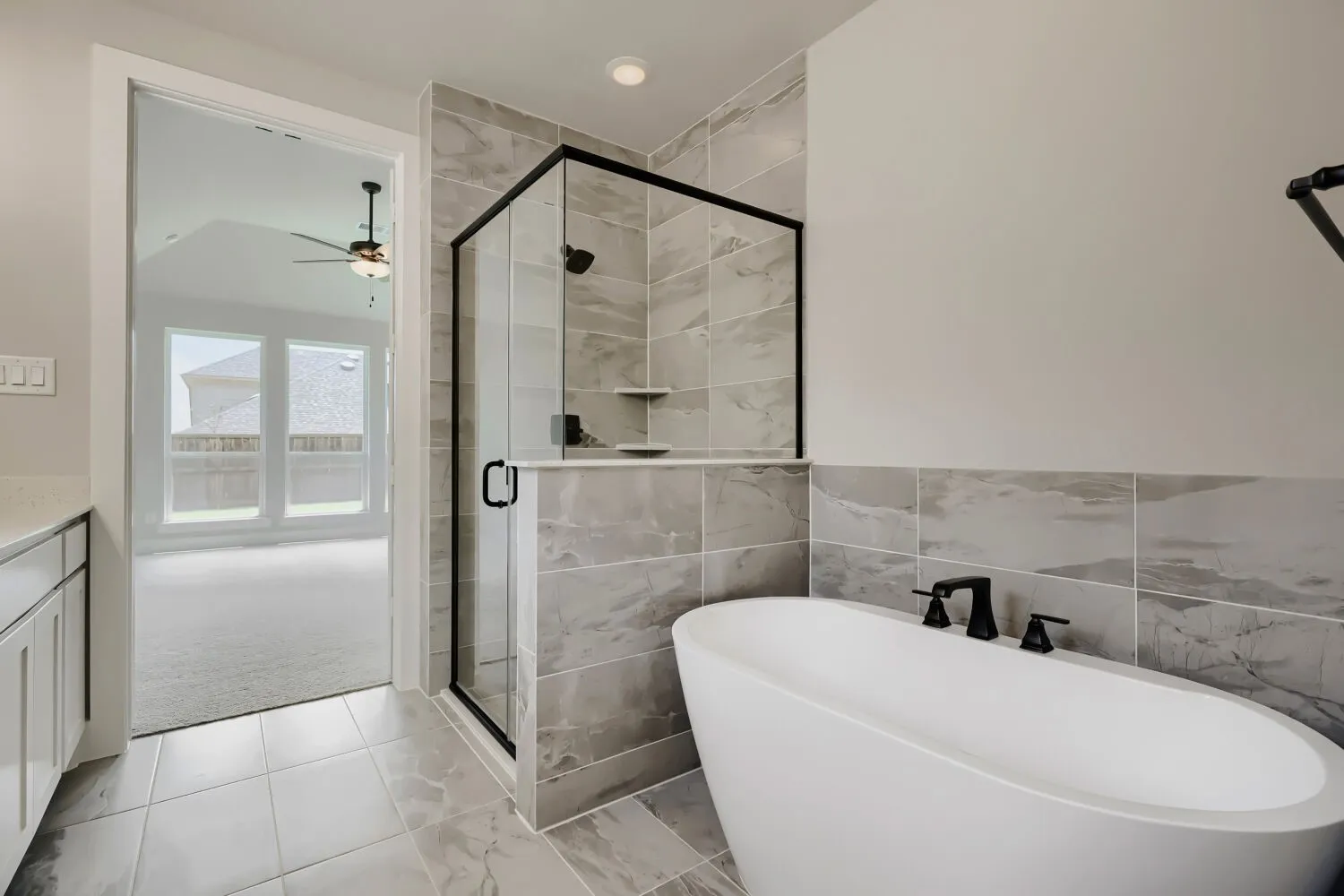 Contemporary bathroom featuring a freestanding soaking tub with matte black fixtures, a glass-enclosed shower with a black frame, and gray marble-look tile flooring and shower surround