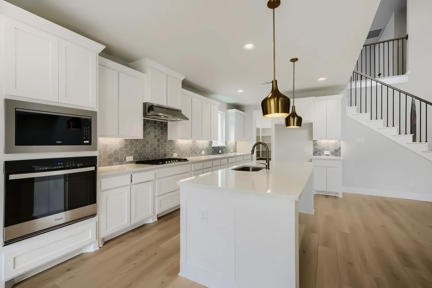 Bright kitchen featuring white cabinetry, a hexagonal tile backsplash, light wood-finish flooring, and a central island with a sink and brass pendant lighting