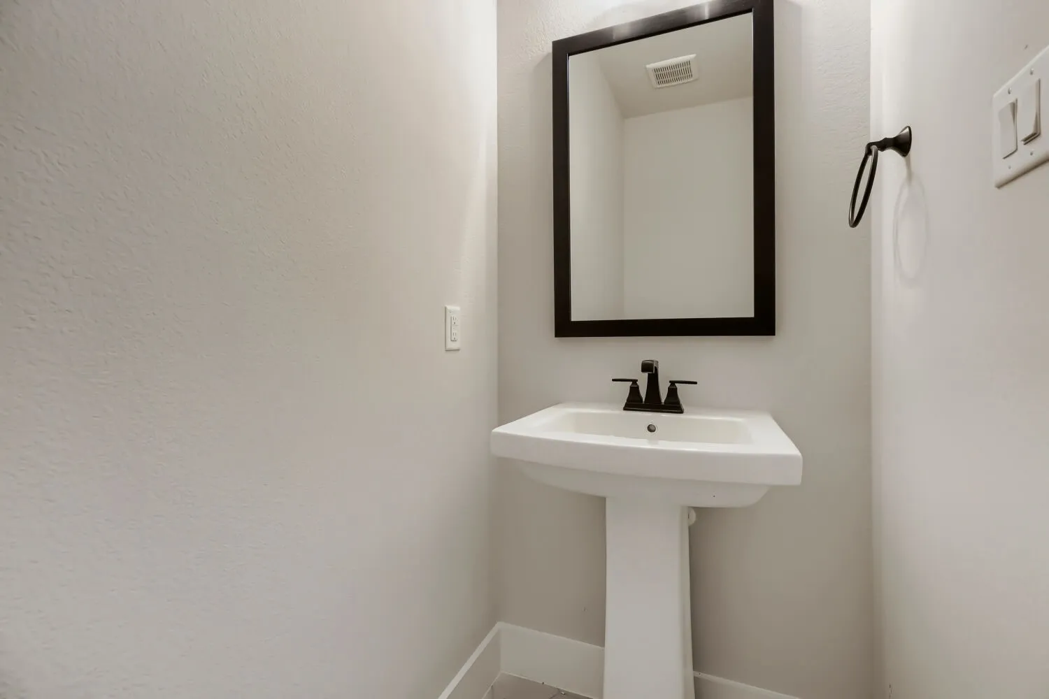 Pedestal sink with a matte black faucet, framed mirror, and a coordinating towel ring