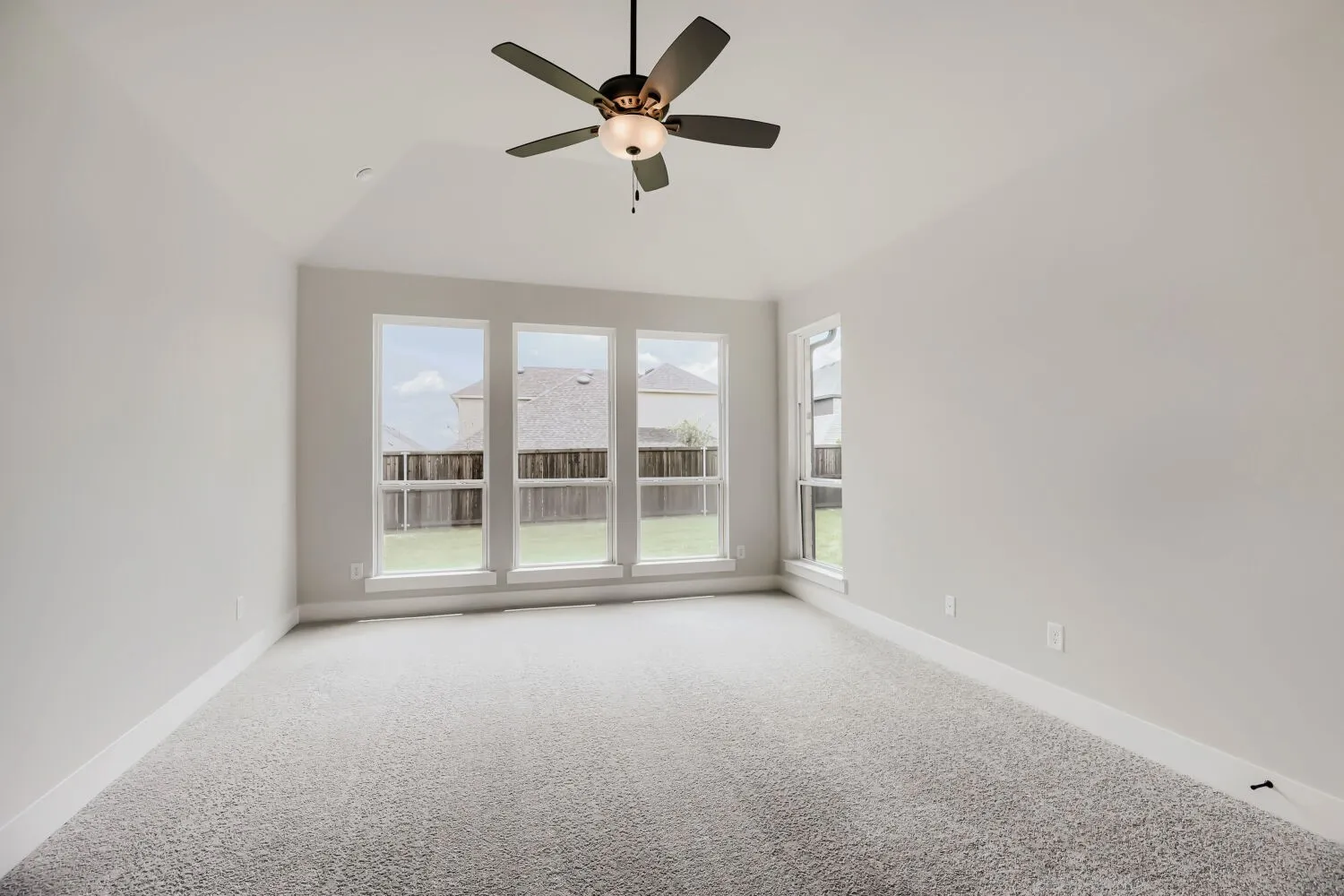 Spacious room featuring light gray carpet, multiple large windows, and a ceiling fan with integrated lighting