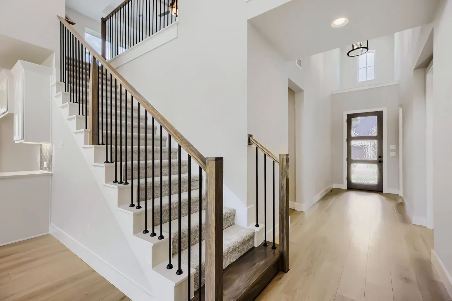 Entryway featuring a carpeted staircase with wood-finish handrails and black metal balusters