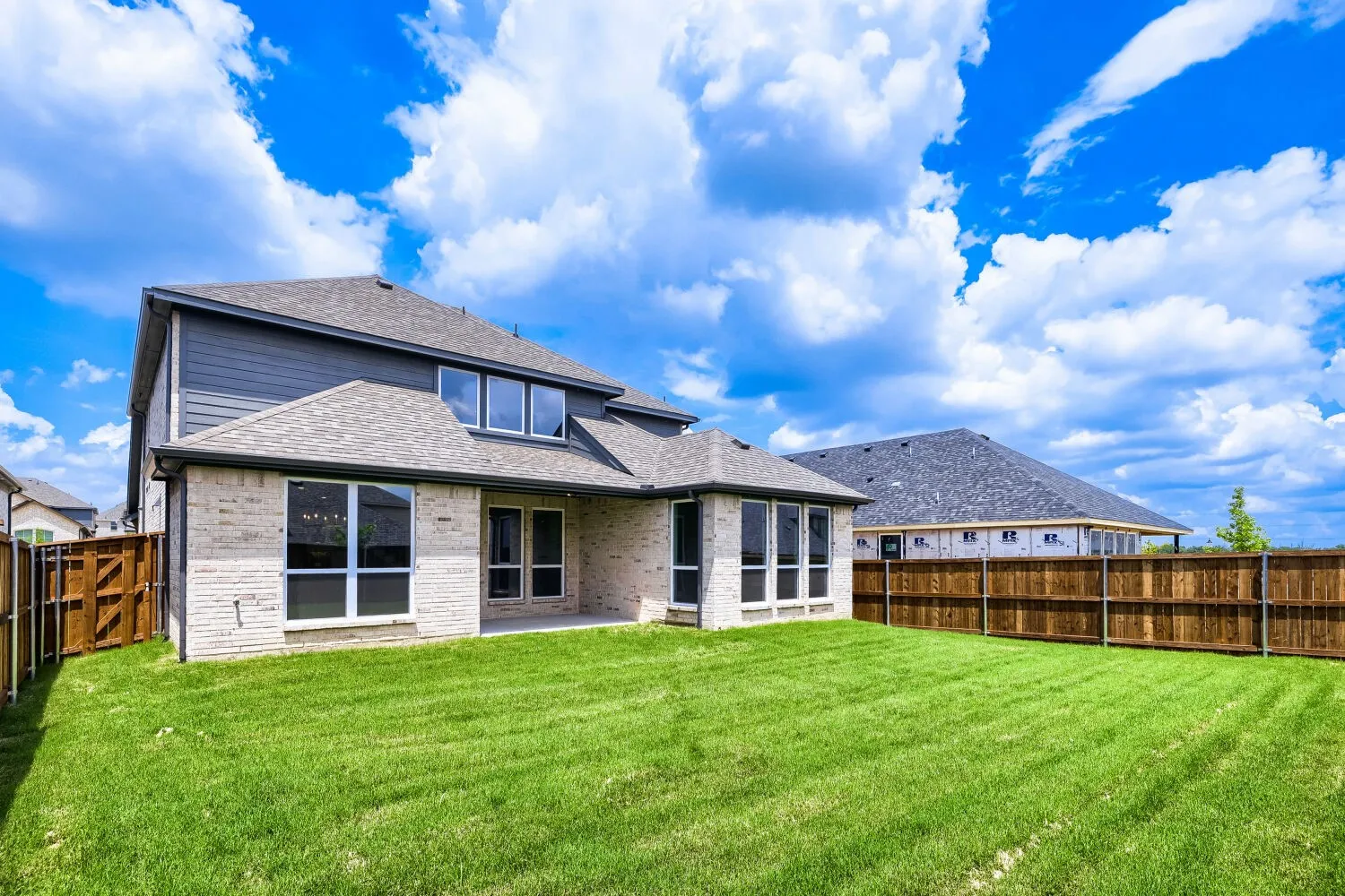 Spacious backyard featuring a large green lawn, a covered patio, and a new privacy fence