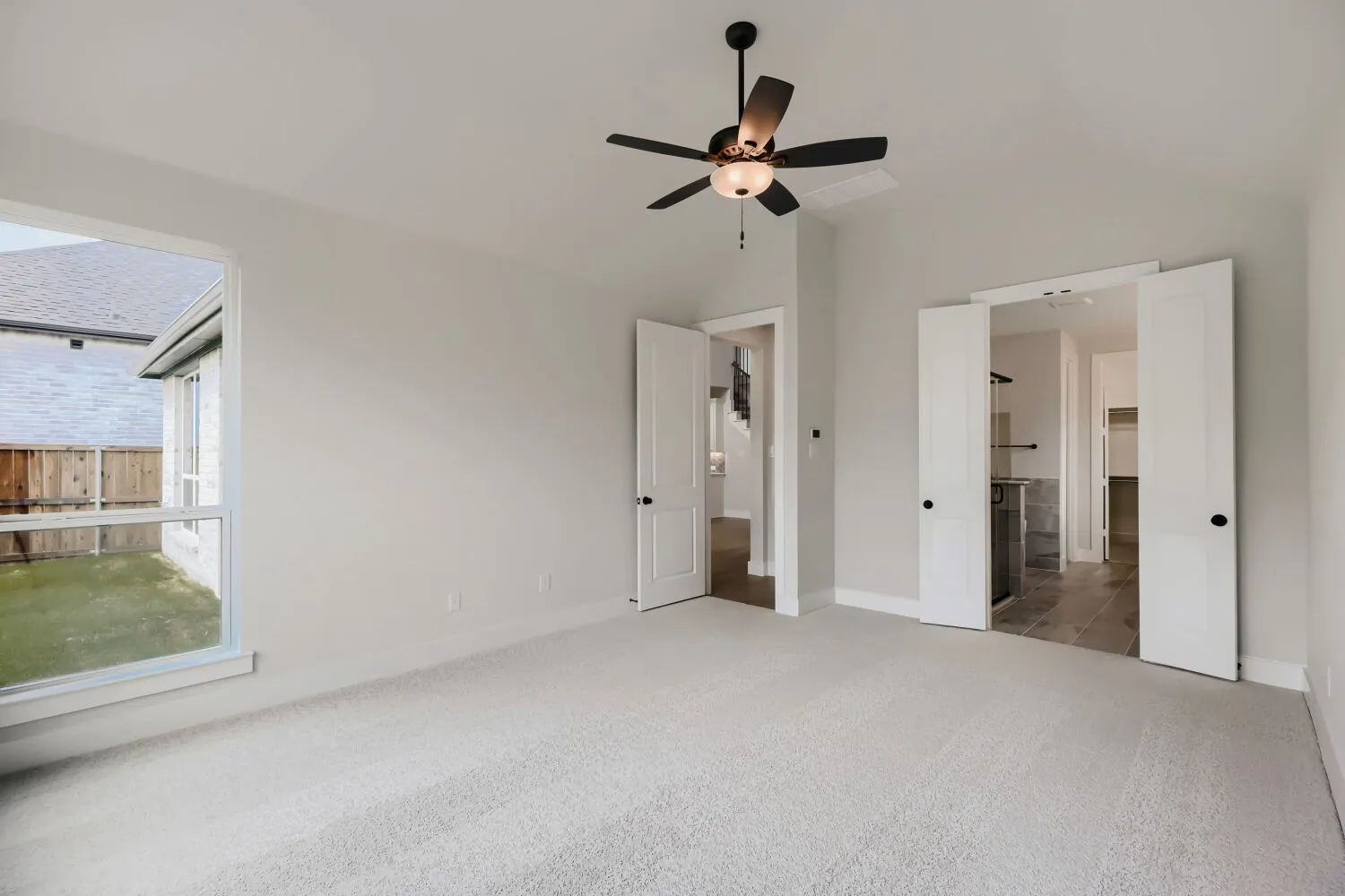 Carpeted room with a large window overlooking a fenced yard
