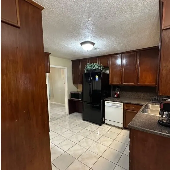 Kitchen with dark countertops, dishwasher, light tile patterned floors, a textured ceiling, and stainless steel microwave