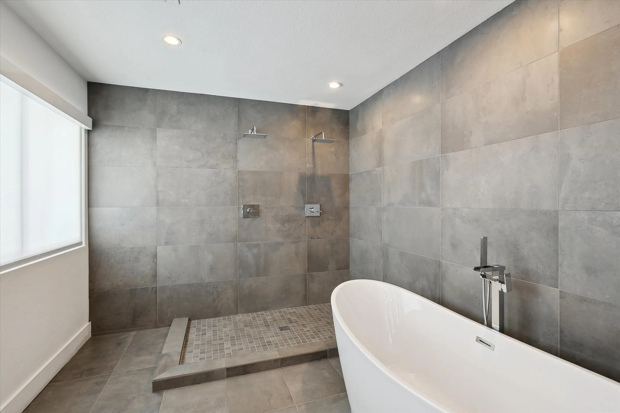 Primary bathroom with, tile flooring and walls, open double shower a freestanding bath.