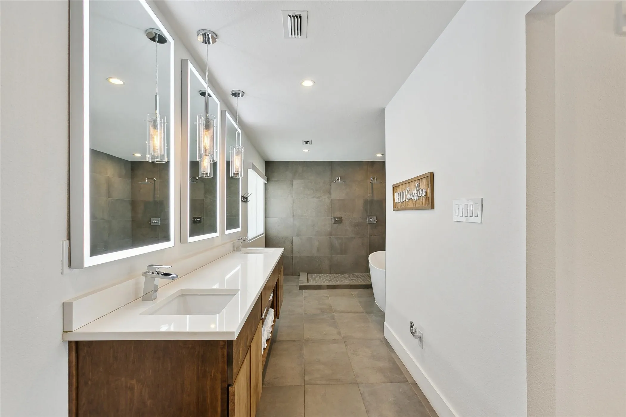 Primary ensuite bathroom with dual sinks, lighted mirrors, and open double shower.
