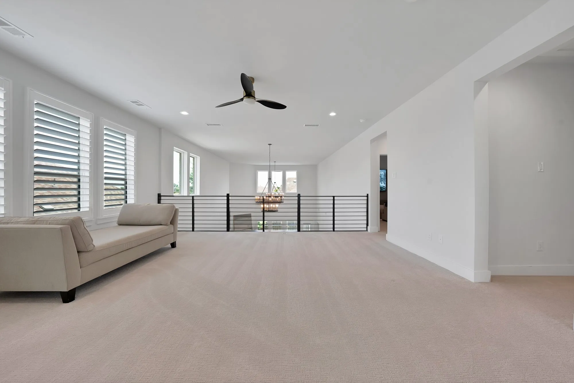 Spacious second-level landing featuring plush carpeting, multiple windows with louvered shutters, a contemporary ceiling fan, recessed lighting, and a modern horizontal railing overlooking the lower level