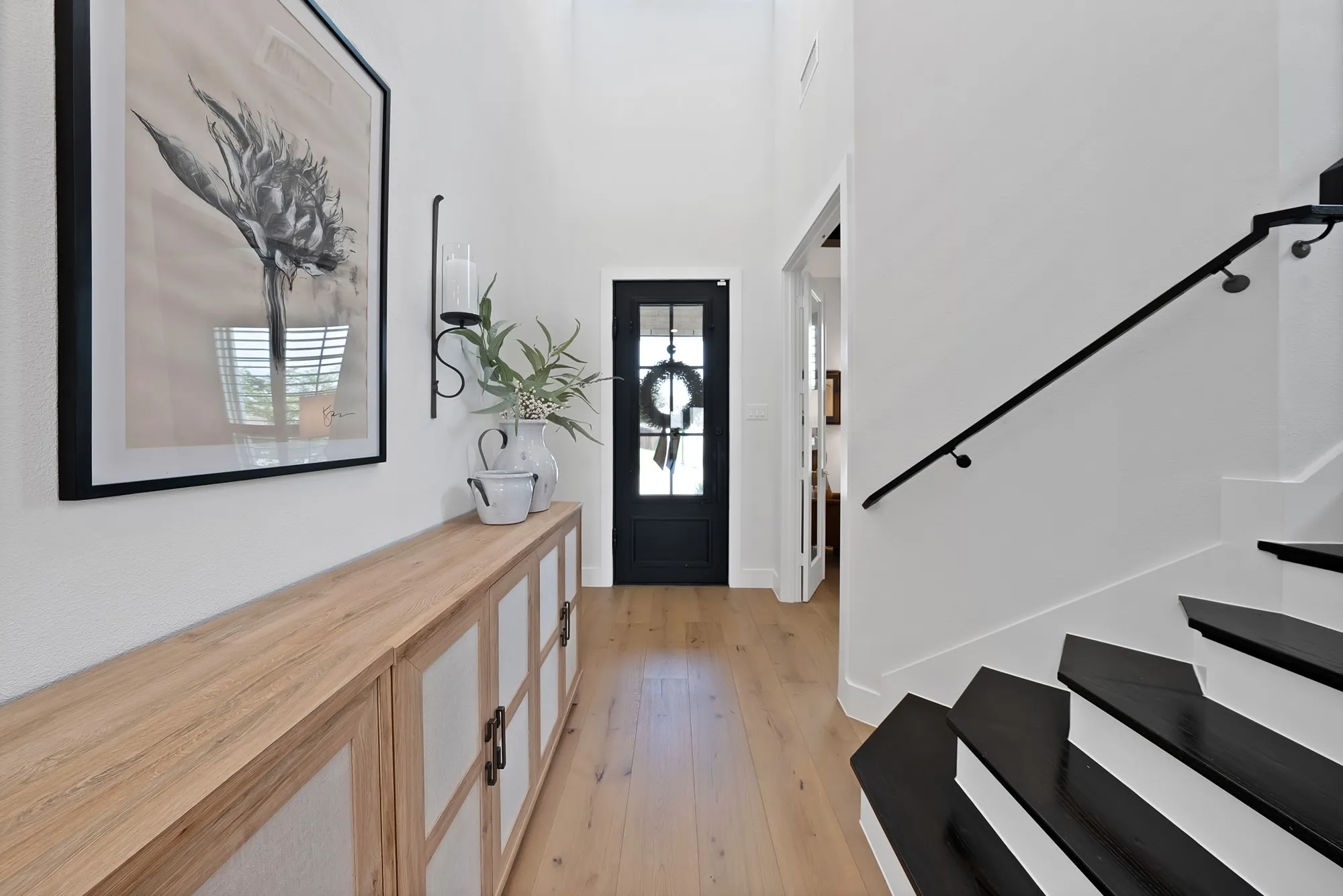 Entryway featuring a dark paneled front door, wood-finish flooring, and a contemporary staircase with dark treads and a black metal handrail