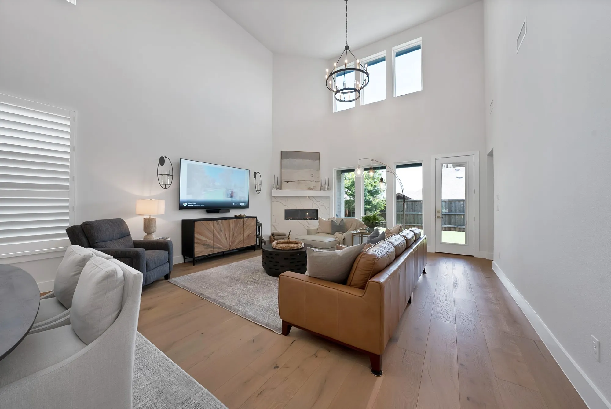 Spacious living area featuring high vaulted ceilings, large windows, light wood-finish flooring, a contemporary chandelier, and a built-in fireplace with a mantel