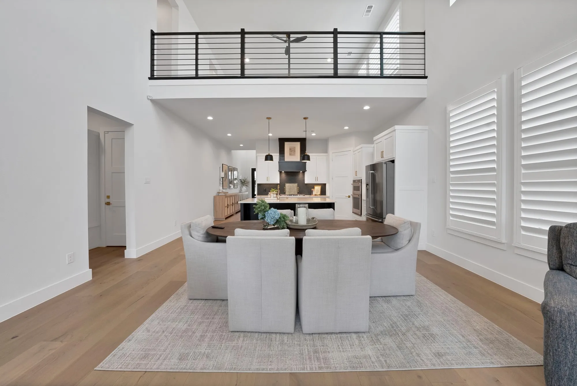Open-concept living space featuring high ceilings, wood-finish flooring, and a second-story balcony with metal railings