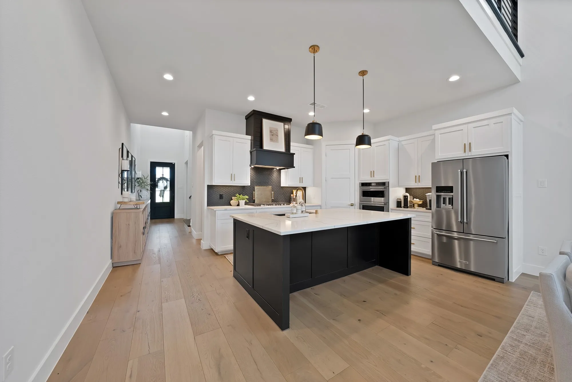 Spacious kitchen featuring a large black island, white shaker cabinetry, stainless steel appliances, and a black range hood