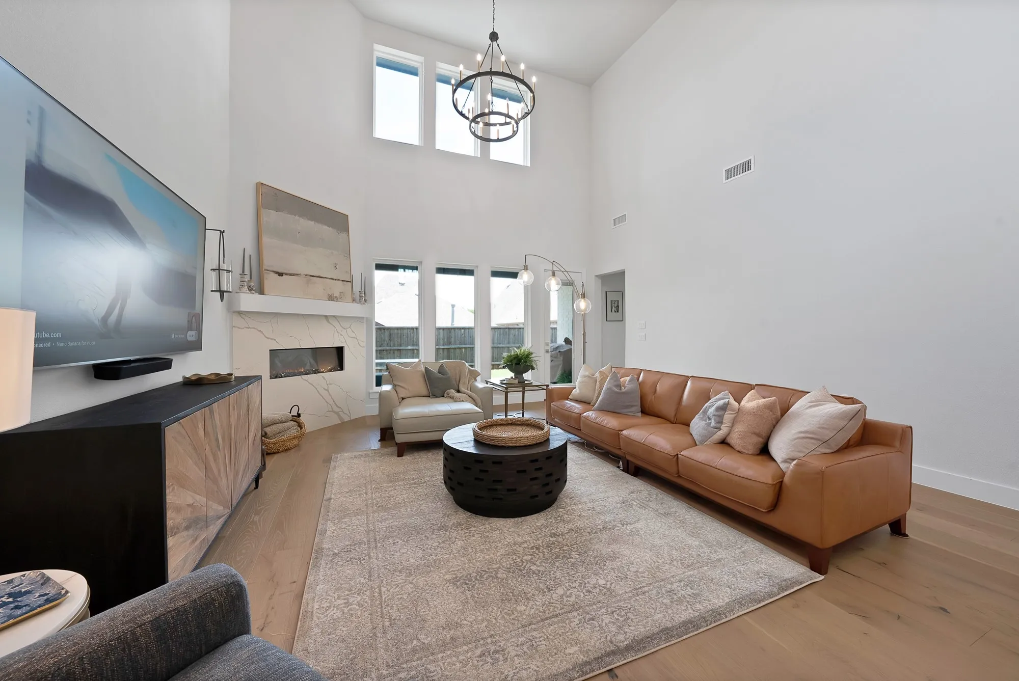 Living area featuring high ceilings, wood-finish flooring, a linear electric fireplace with a decorative stone surround, and large windows with transoms