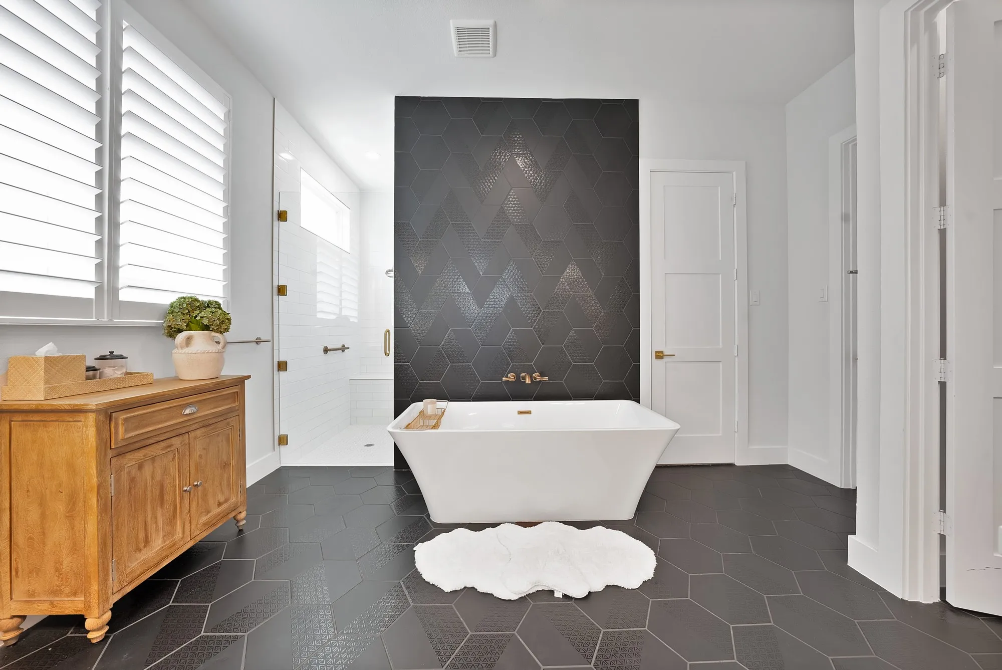 Freestanding soaking tub with brass fixtures set against a dark hexagonal tile accent wall