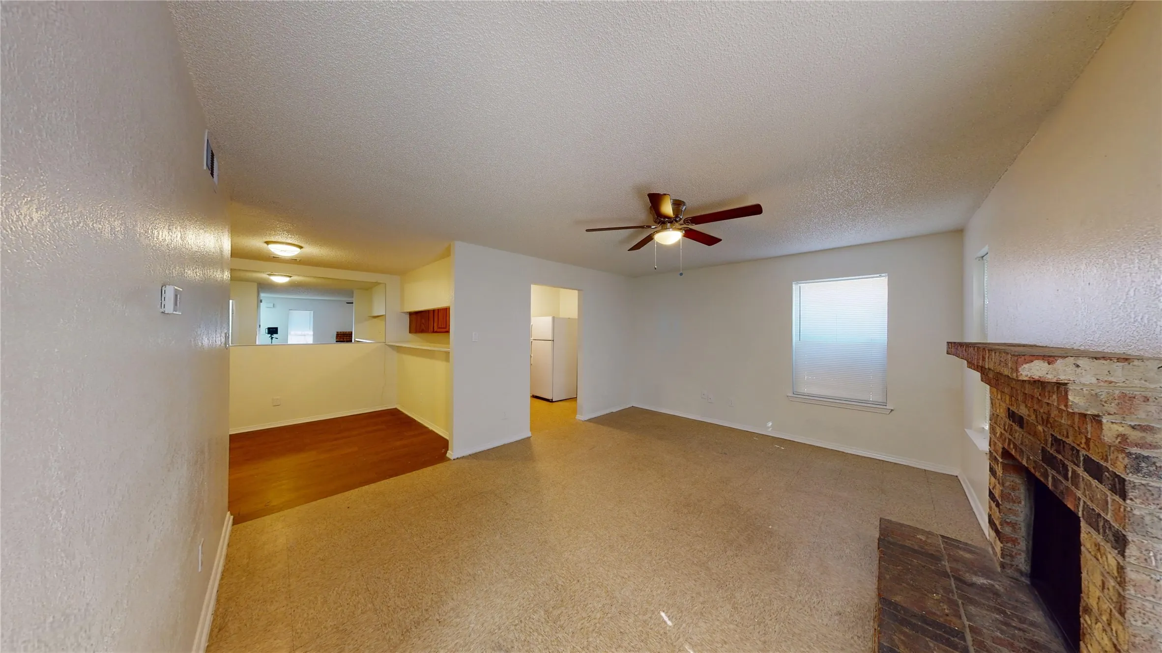 Unfurnished living room with a textured wall, a textured ceiling, a brick fireplace, and ceiling fan
