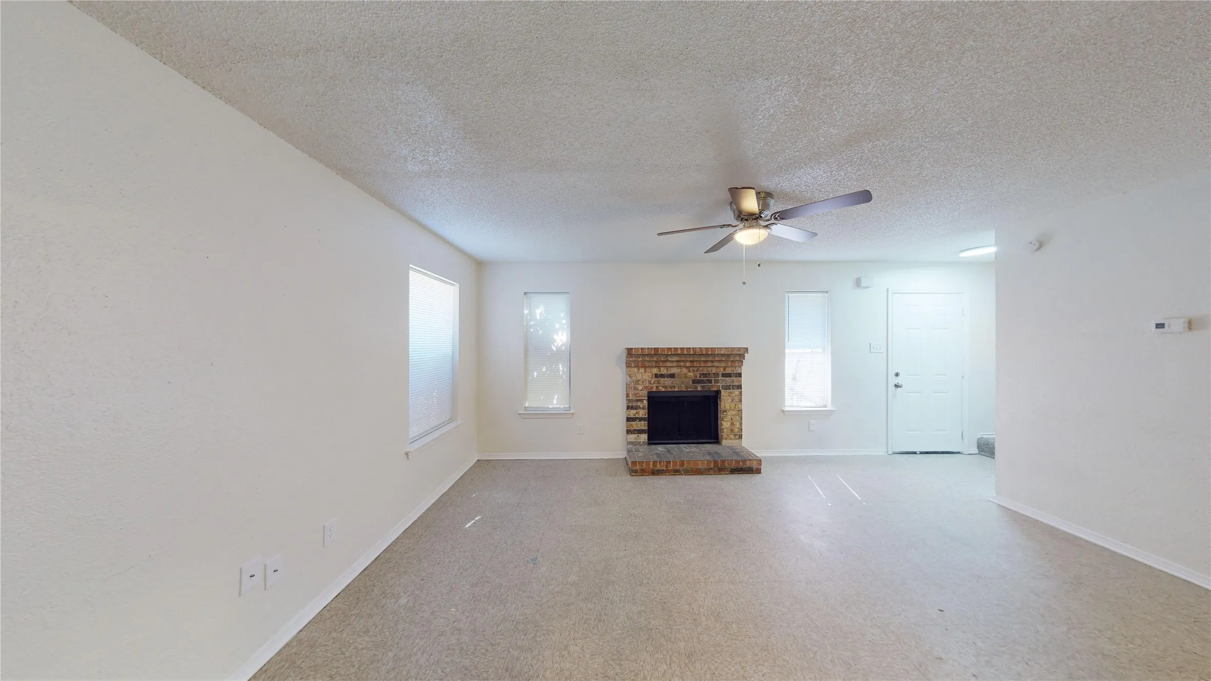 Unfurnished living room featuring a brick fireplace, a textured ceiling, and ceiling fan