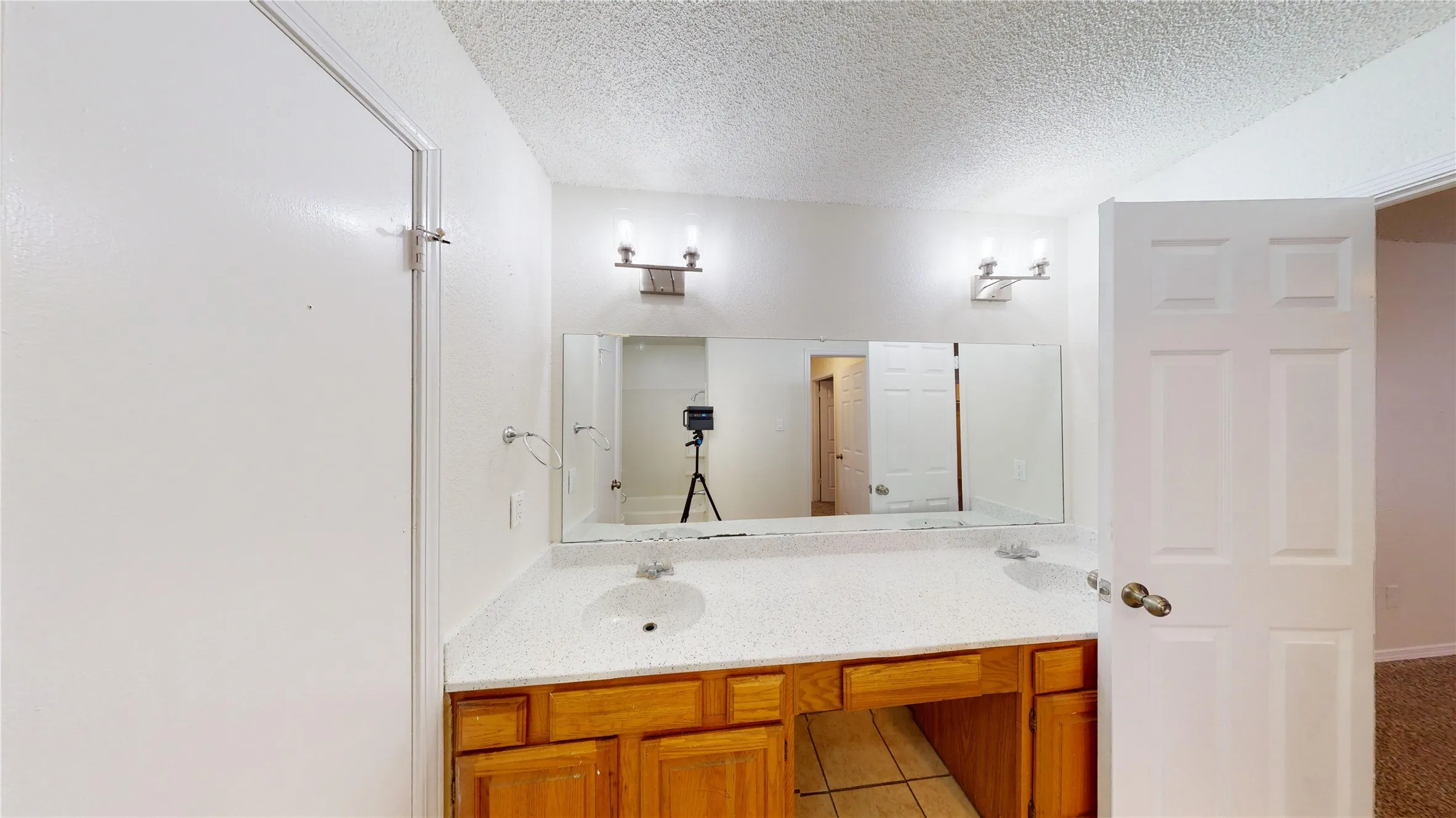 Bathroom with double vanity, a textured ceiling, and light tile patterned floors
