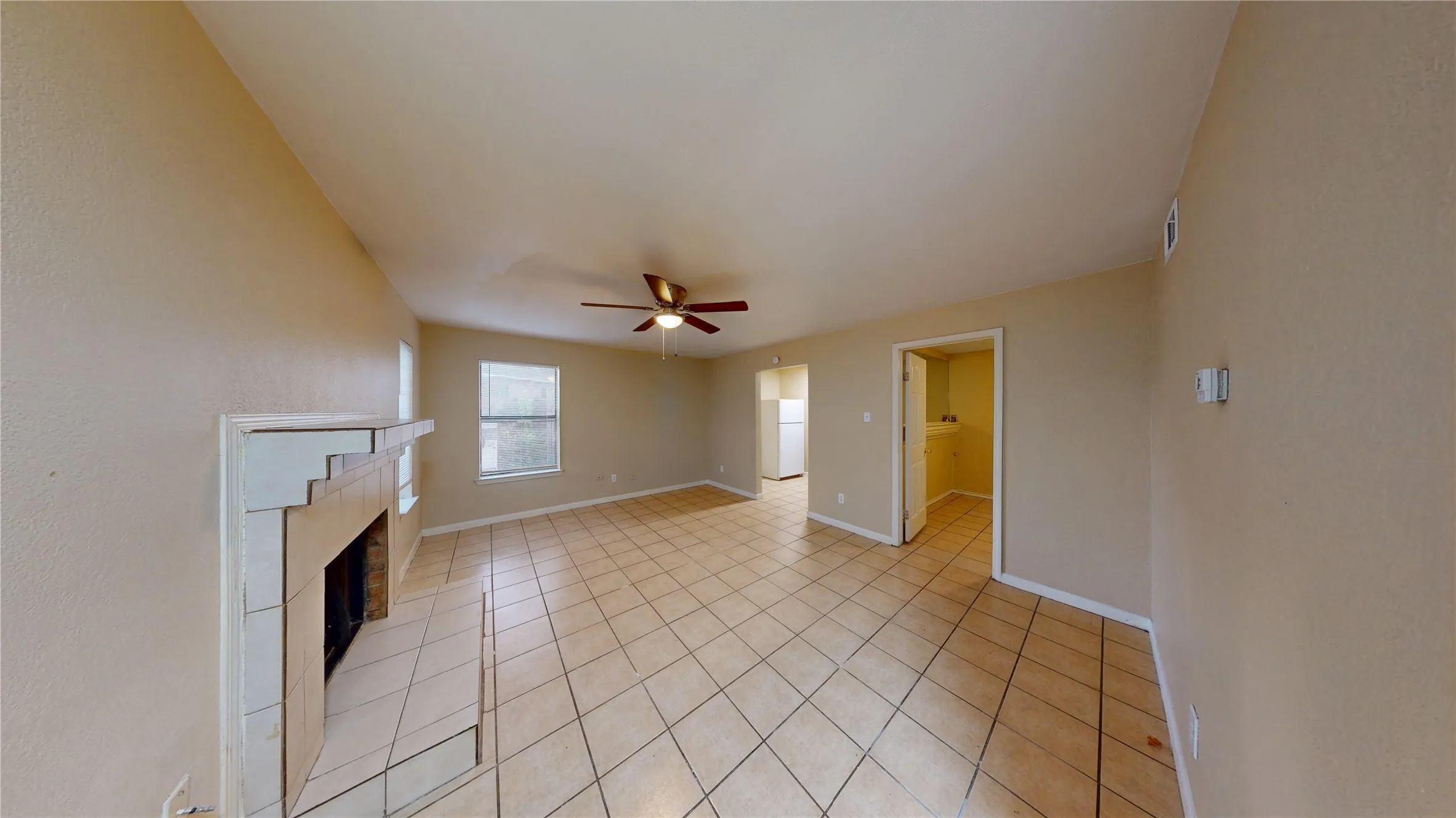 Unfurnished living room with a tiled fireplace, light tile patterned floors, and a ceiling fan