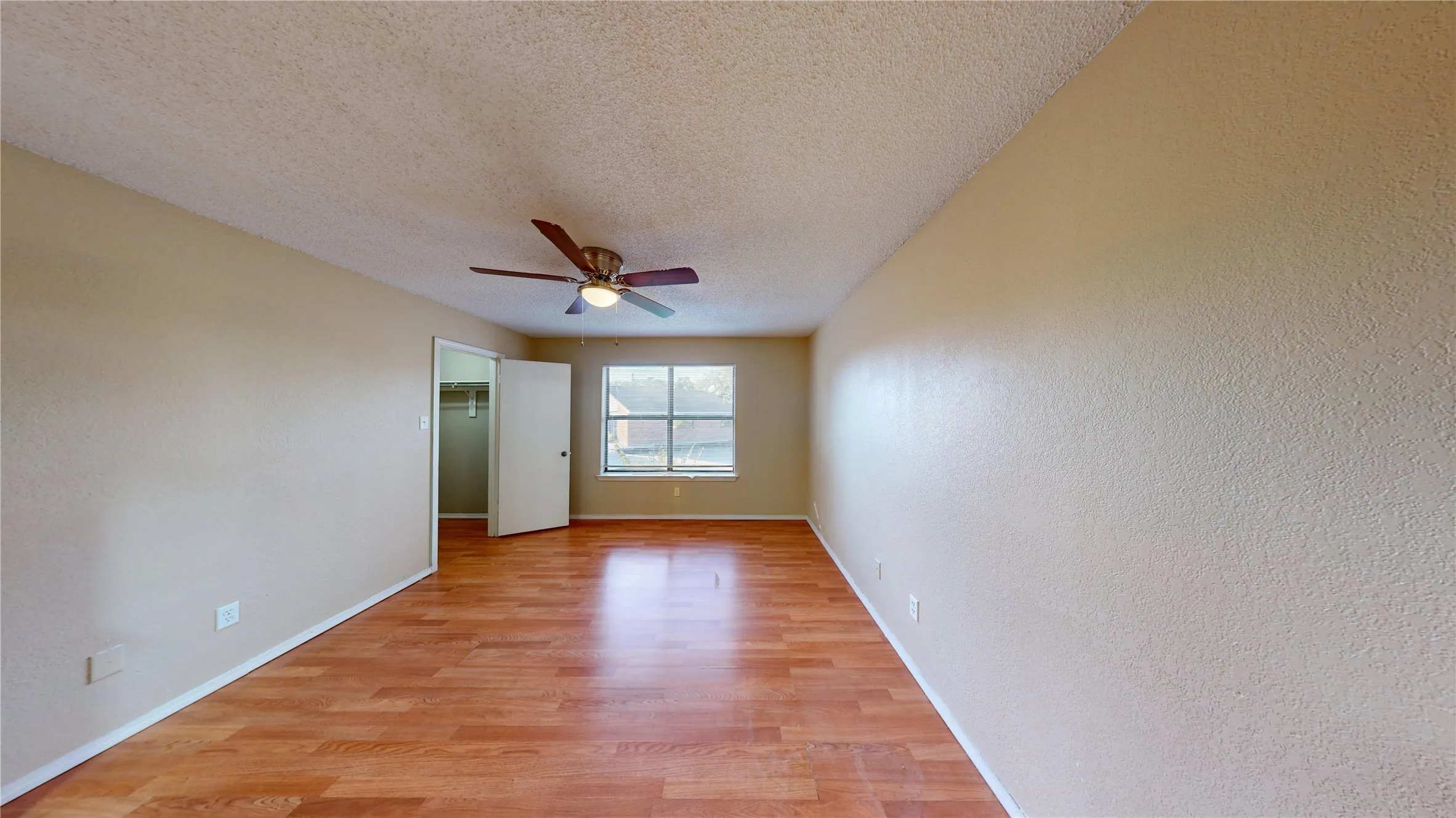 Unfurnished bedroom featuring light wood-style flooring, a textured ceiling, a spacious closet, ceiling fan, and a textured wall