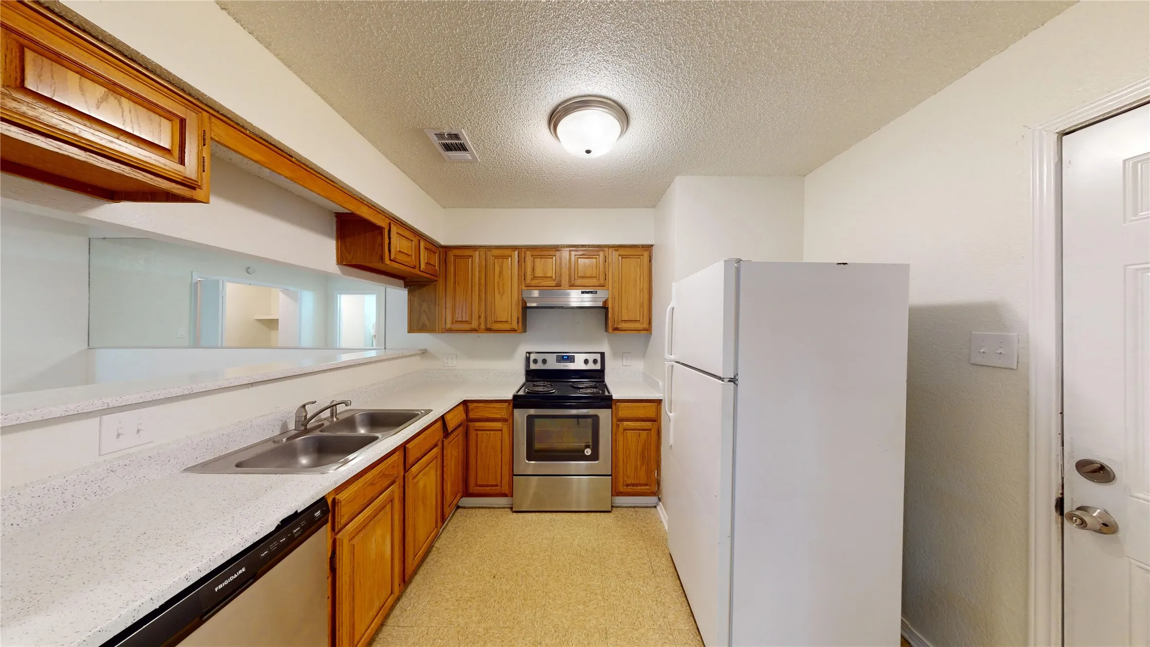 Kitchen featuring appliances with stainless steel finishes, a textured ceiling, brown cabinets, under cabinet range hood, and light floors