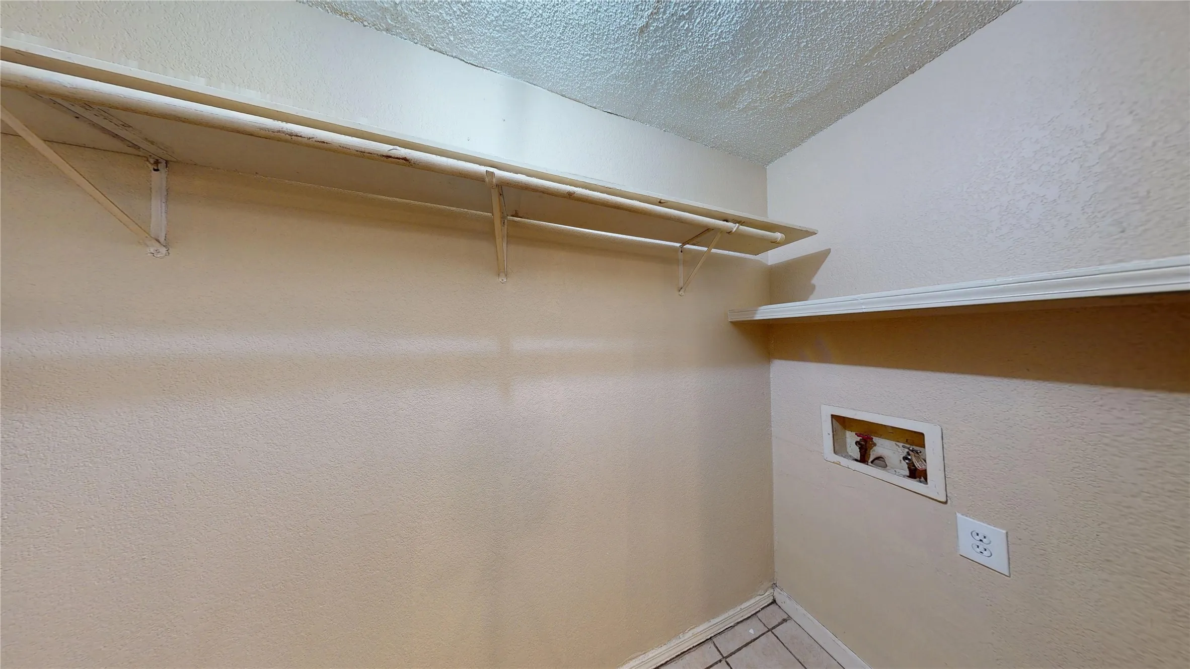 Laundry area with a textured ceiling, a textured wall, washer hookup, and light tile patterned flooring
