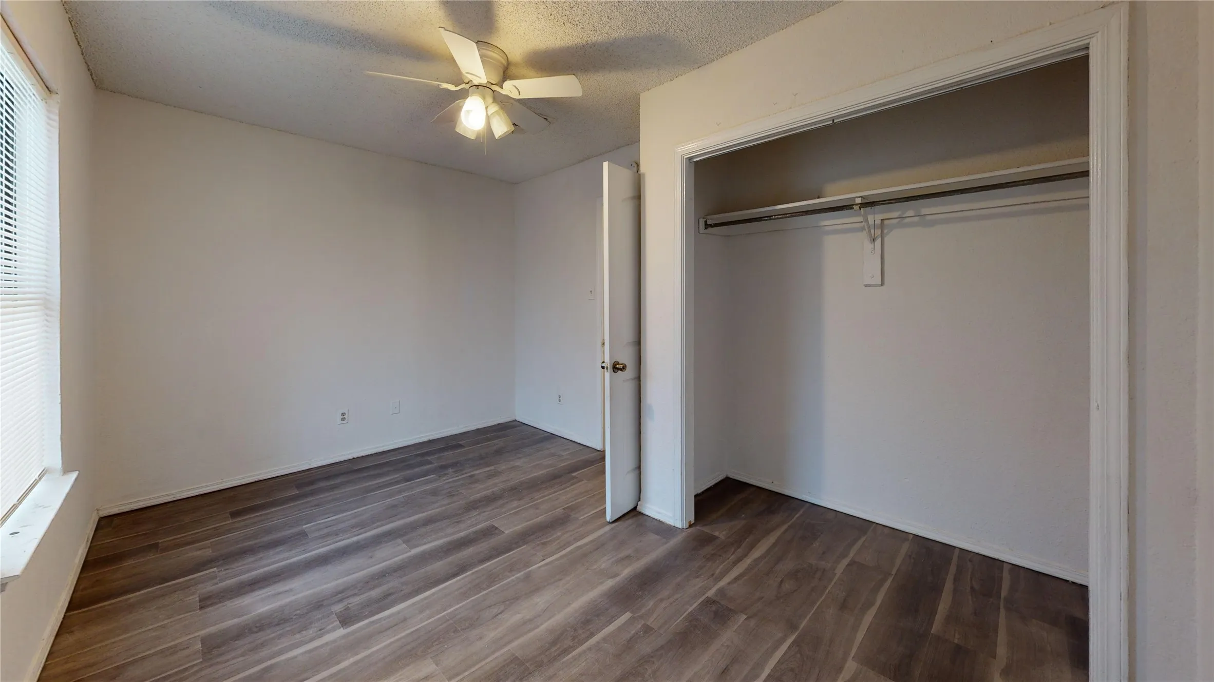 Unfurnished bedroom with a textured ceiling, dark wood-type flooring, ceiling fan, and a closet