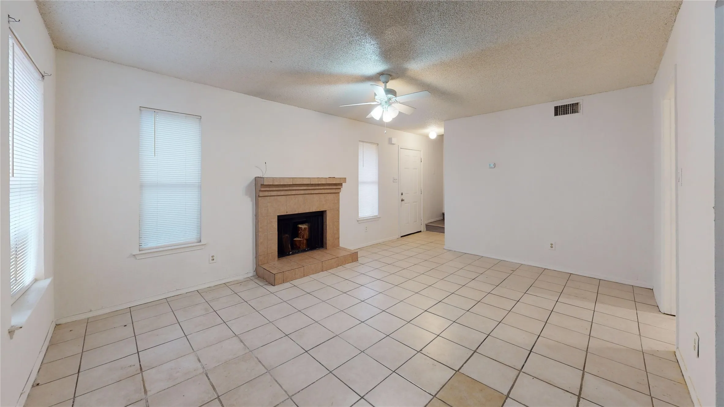 Unfurnished living room with a textured ceiling, a tile fireplace, ceiling fan, and light tile patterned flooring