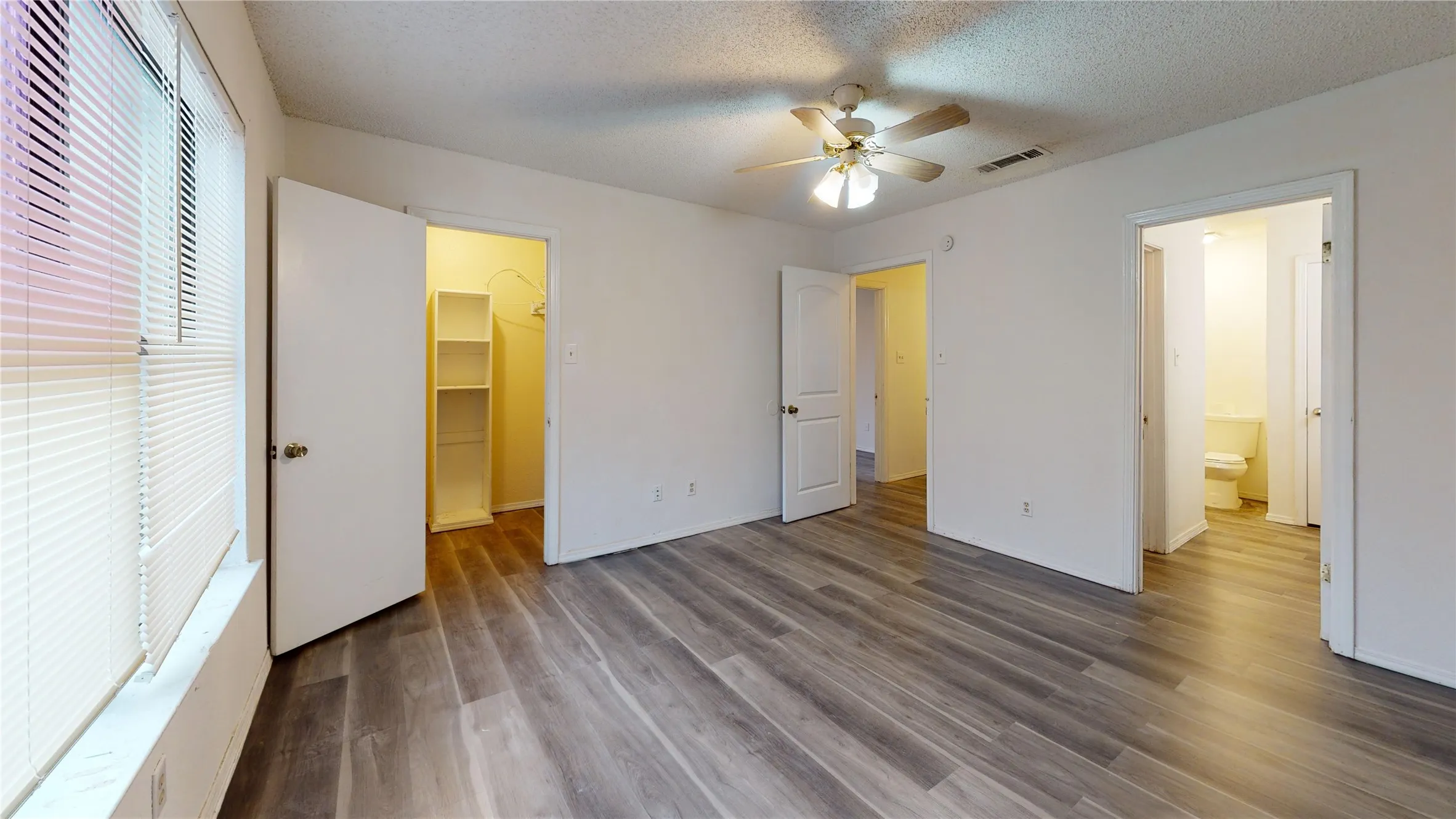 Unfurnished bedroom with a walk in closet, dark wood finished floors, ceiling fan, and a textured ceiling